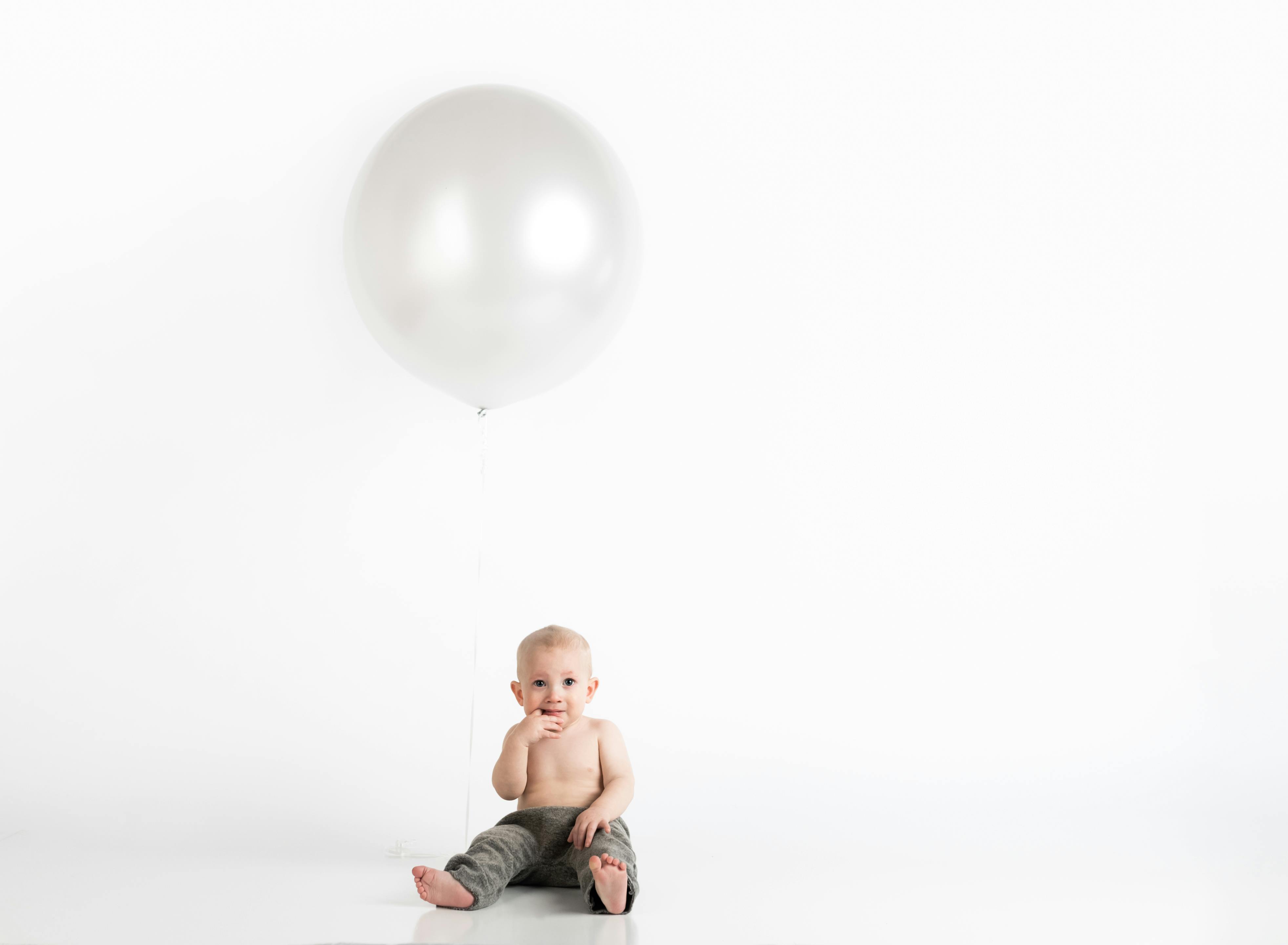 A baby sits on the floor next to a large white balloon.