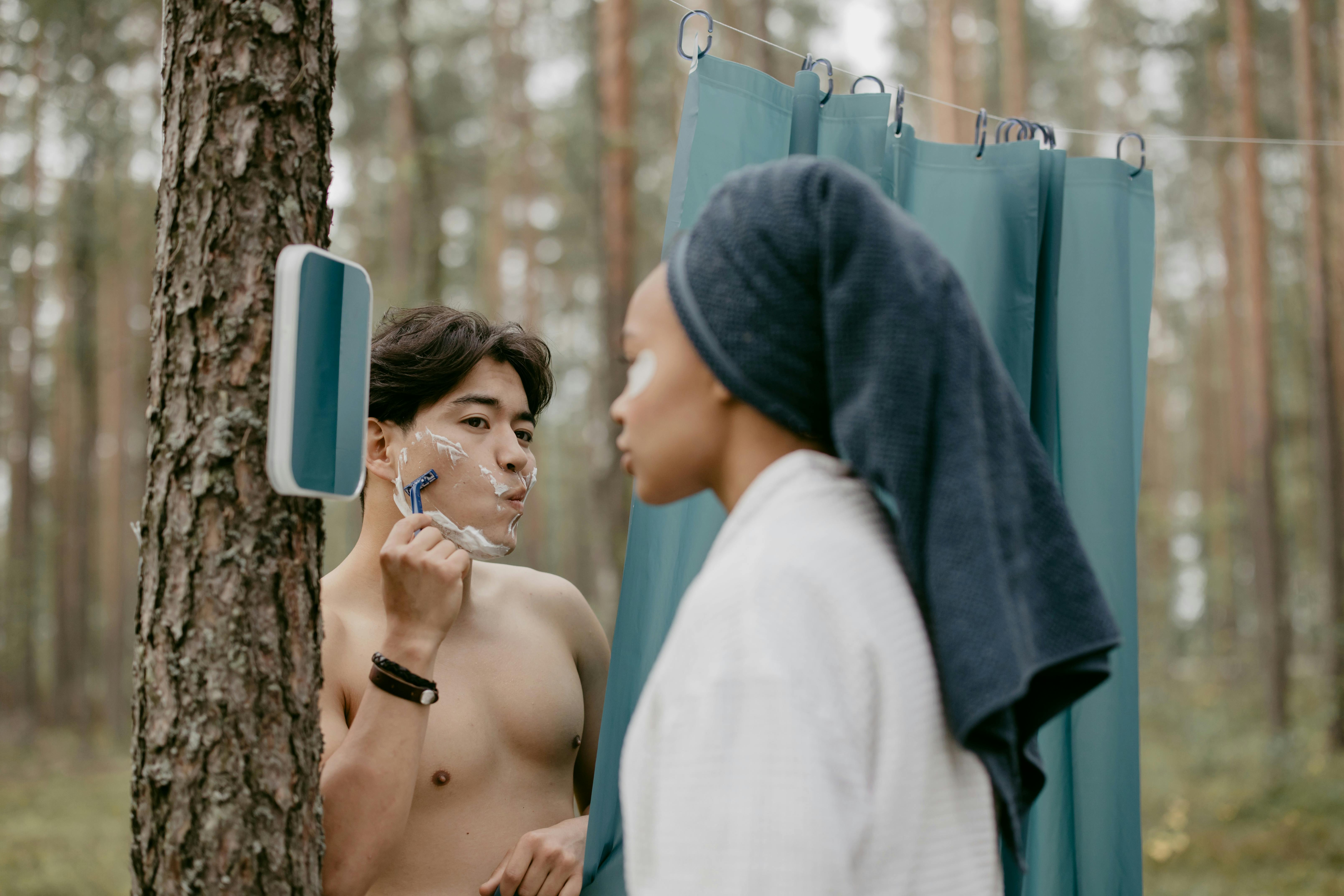 Two people grooming outdoors, one shaving, one with towel.
