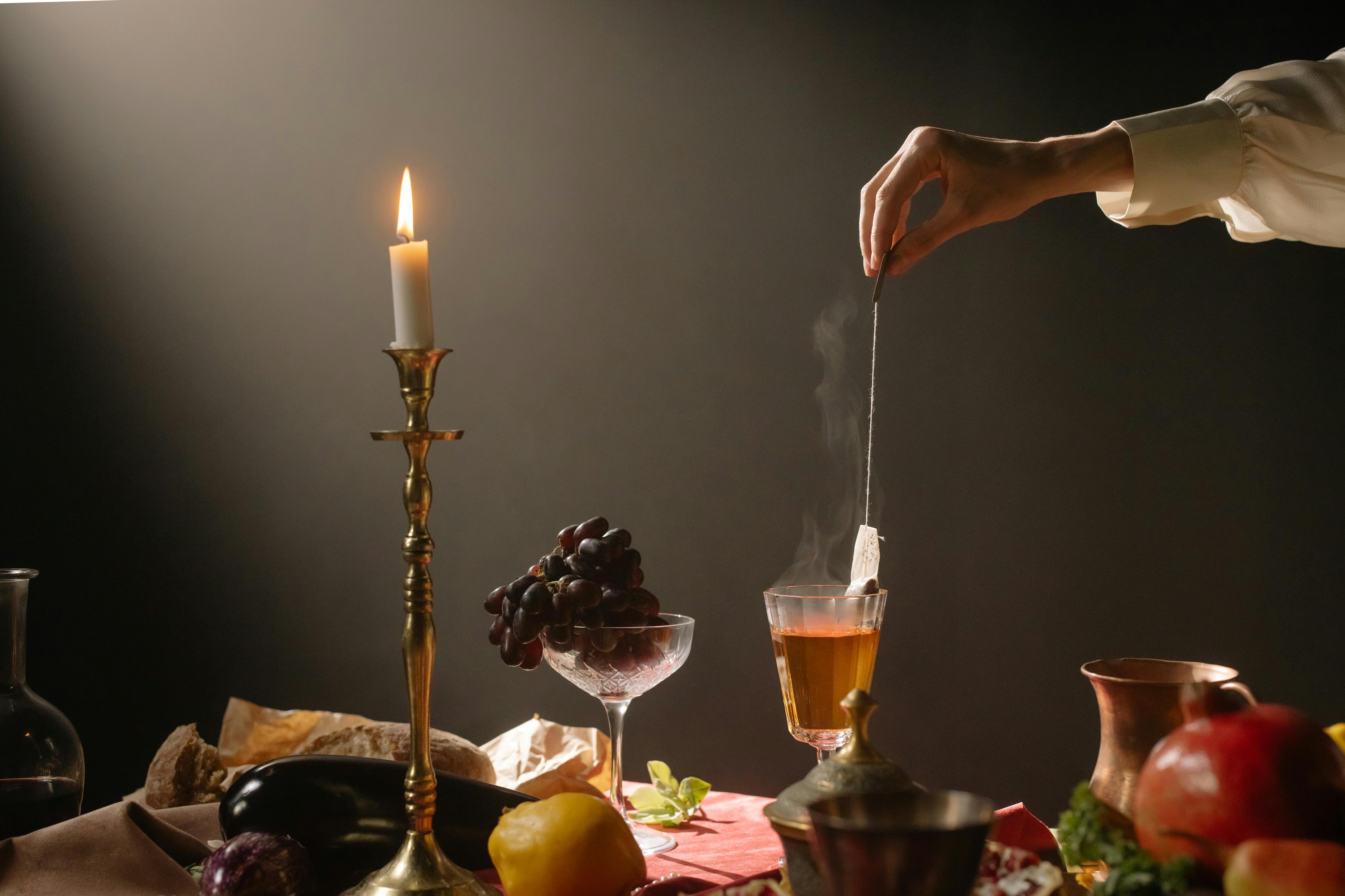 Candlelit table with tea, fruit, bread, and elegant hand.