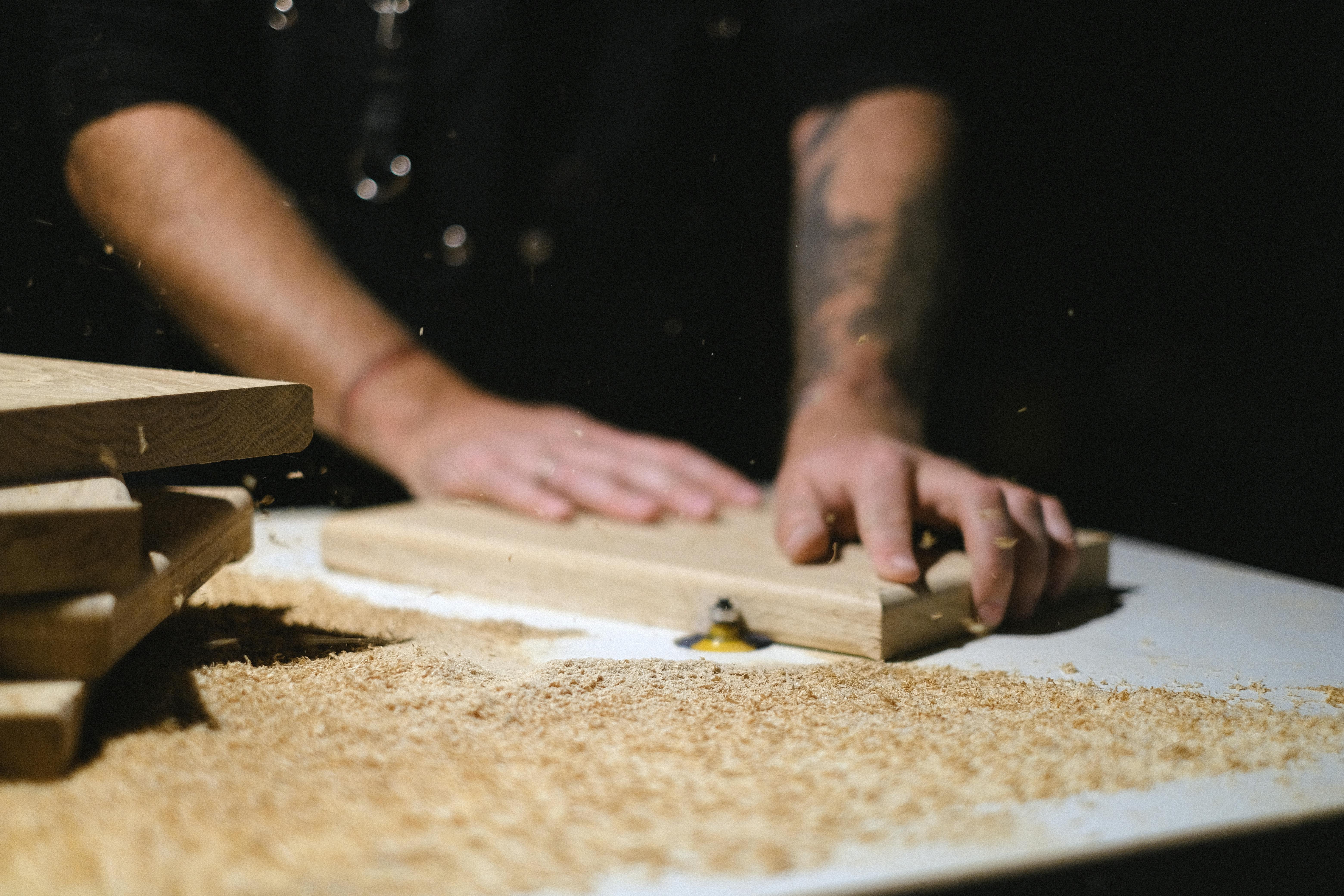 Person sanding wood, sawdust scattered on work surface, focused hands.