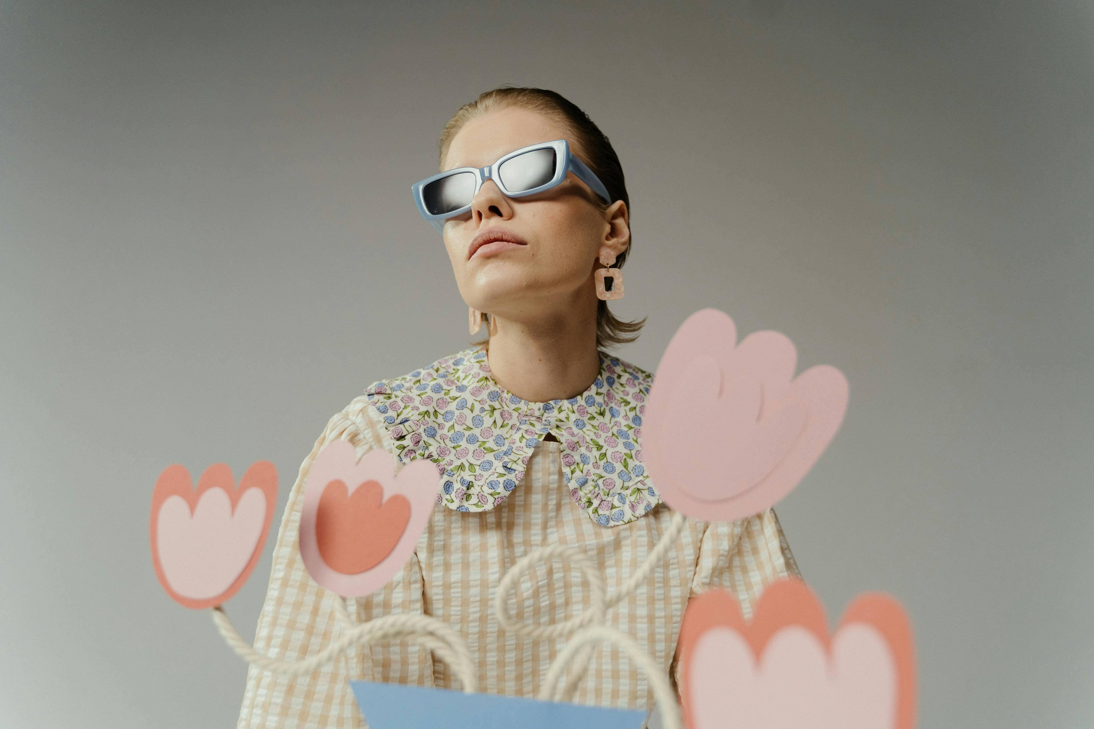 Person wearing sunglasses and a floral collar shirt with paper flowers.