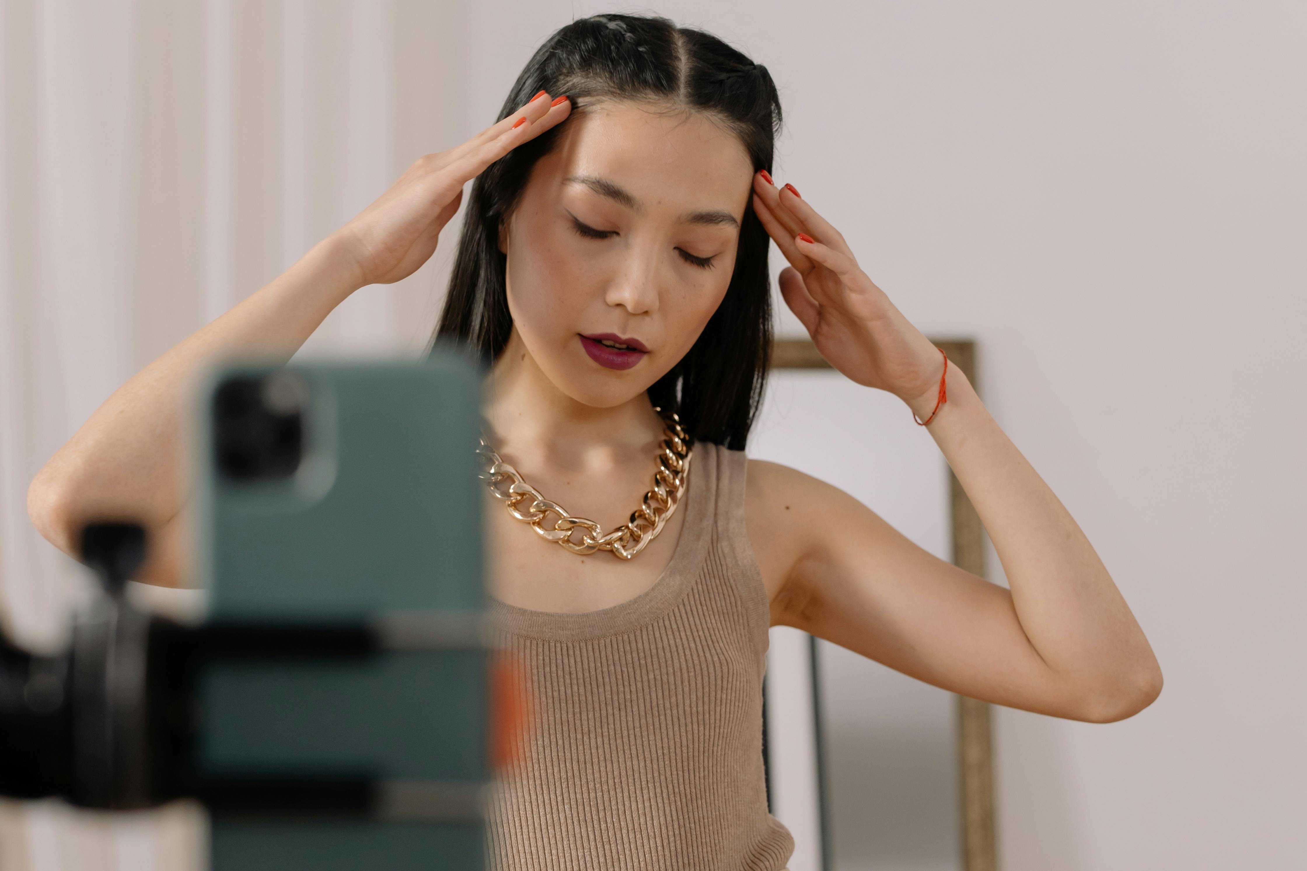 Person posing in front of smartphone, hands near head, indoors.