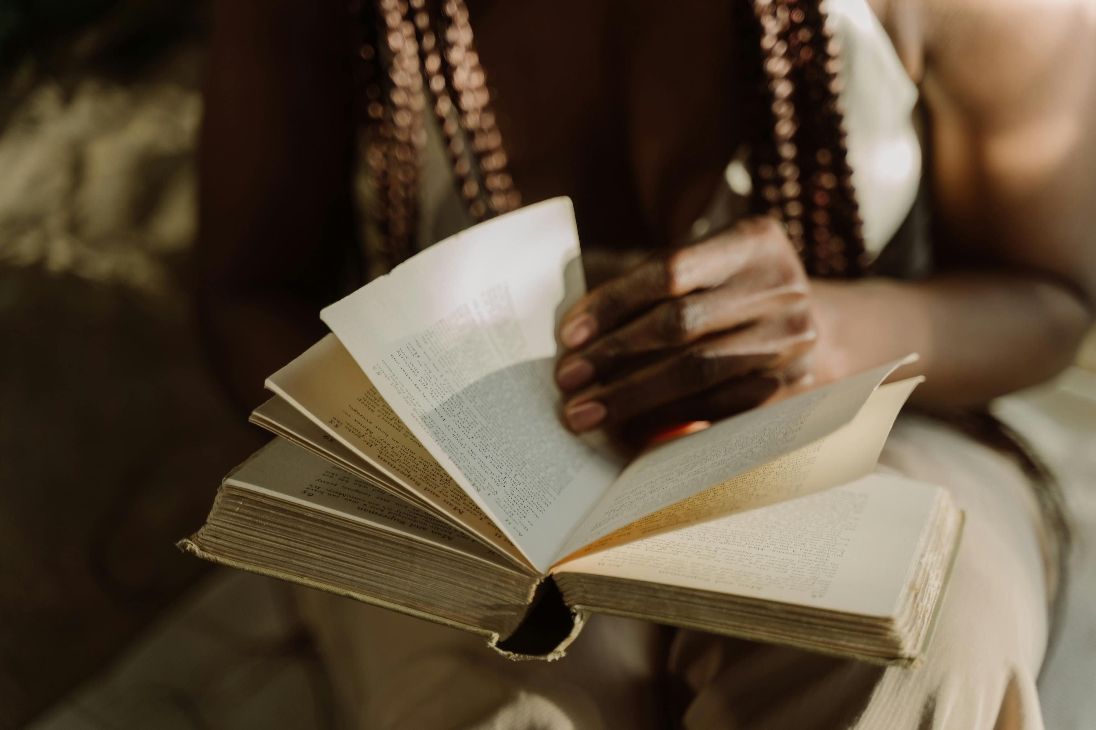 Person turning pages of an old book in soft light.