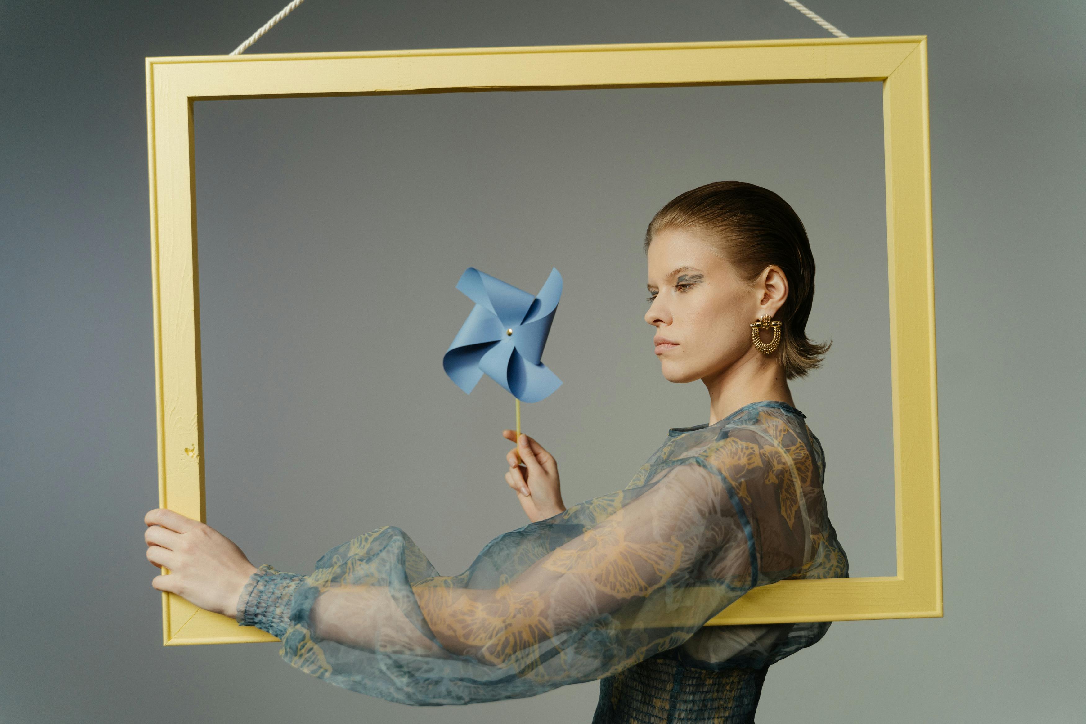 Person holding a blue pinwheel inside a yellow frame.
