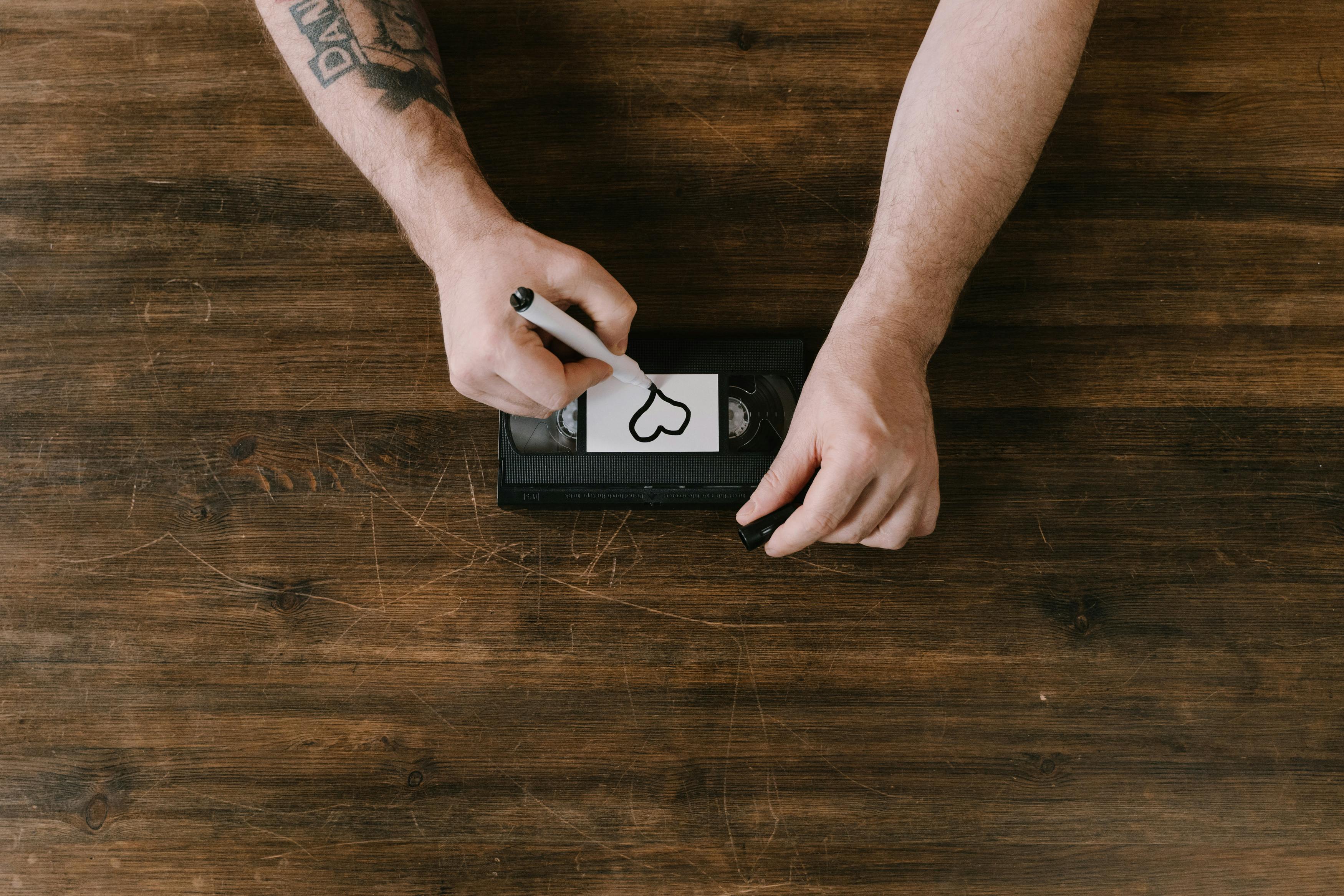 Person drawing a heart on a VHS tape label.