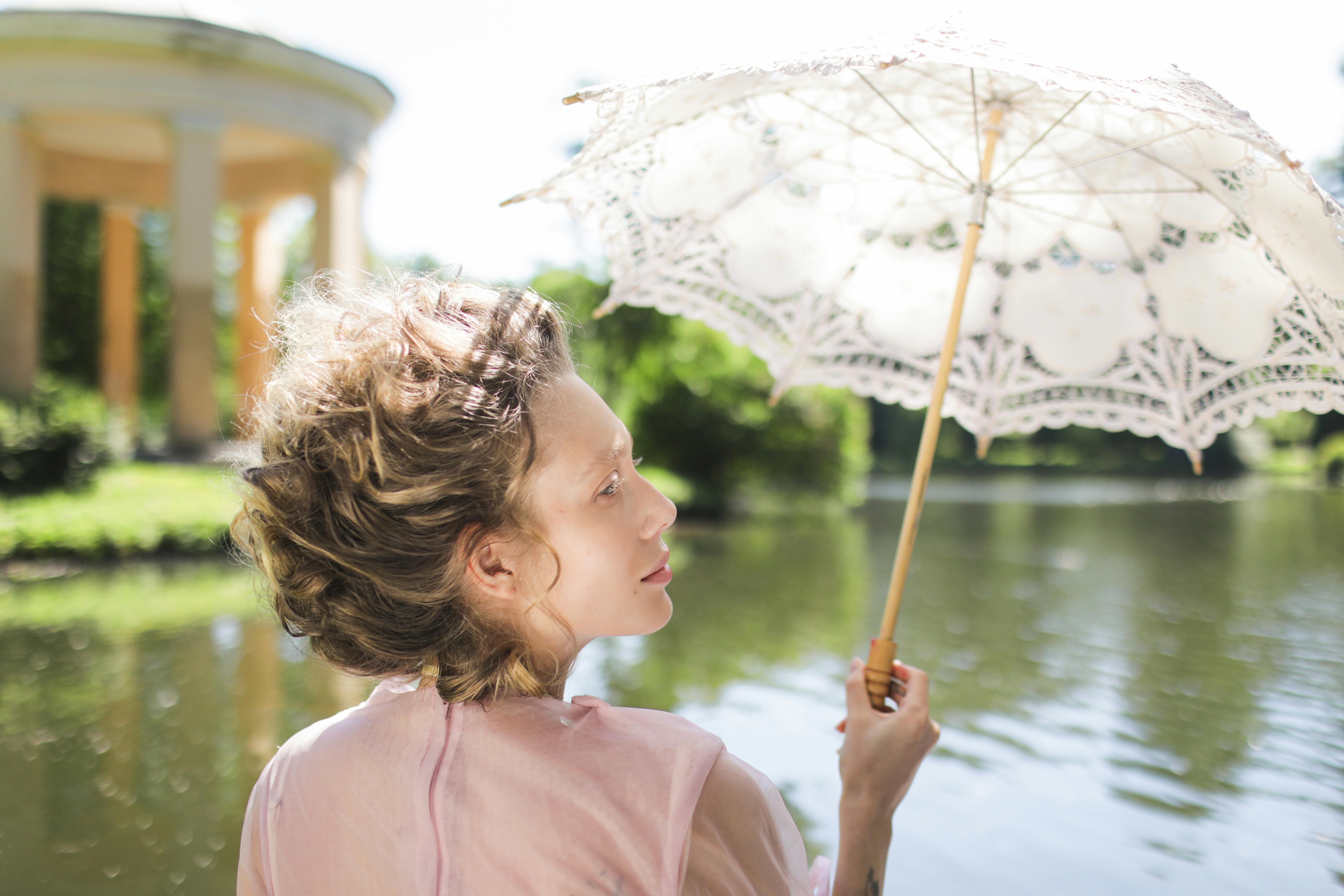 A person holds a delicate lace umbrella by a tranquil lake.