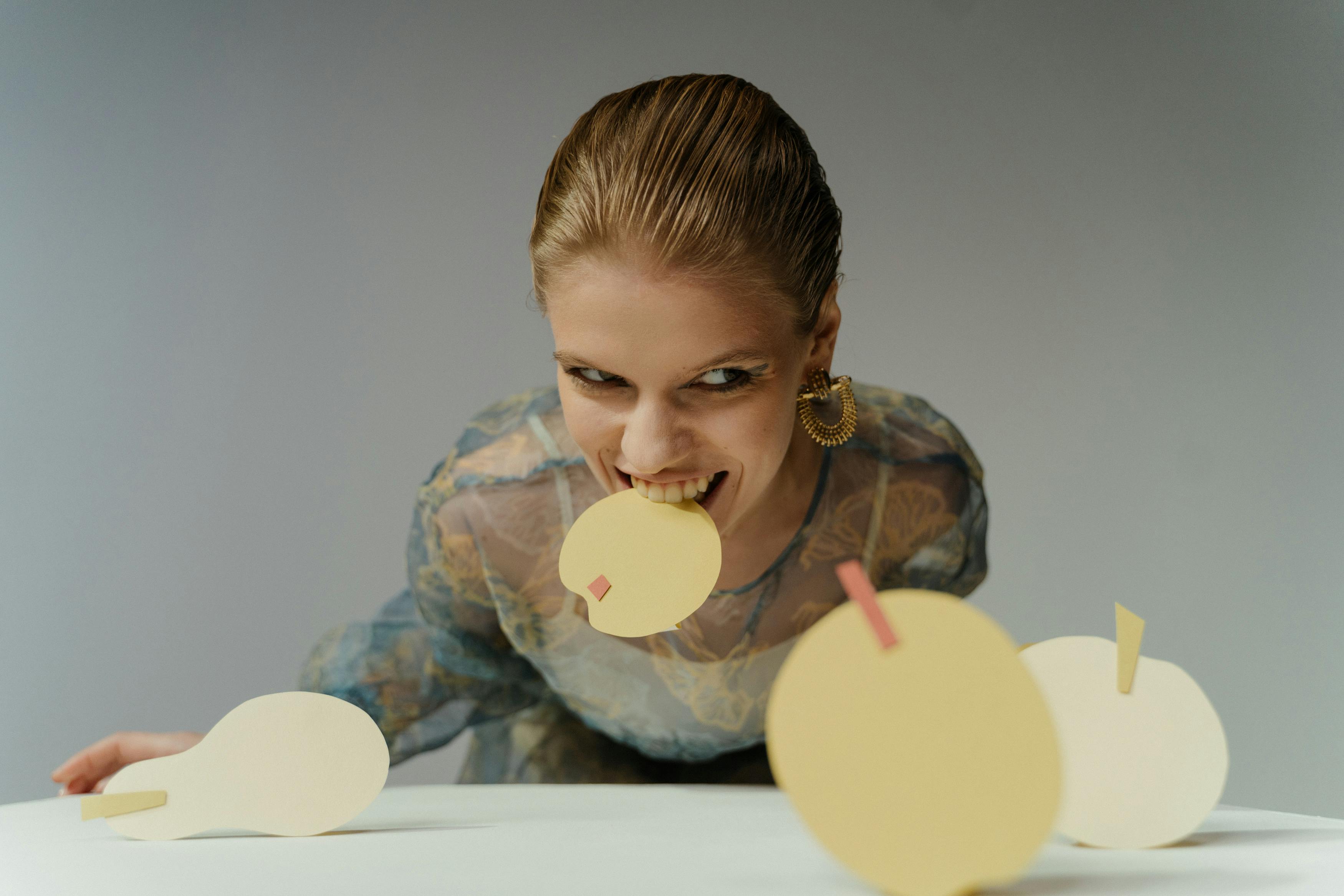Person biting a yellow paper circle with a pink square.