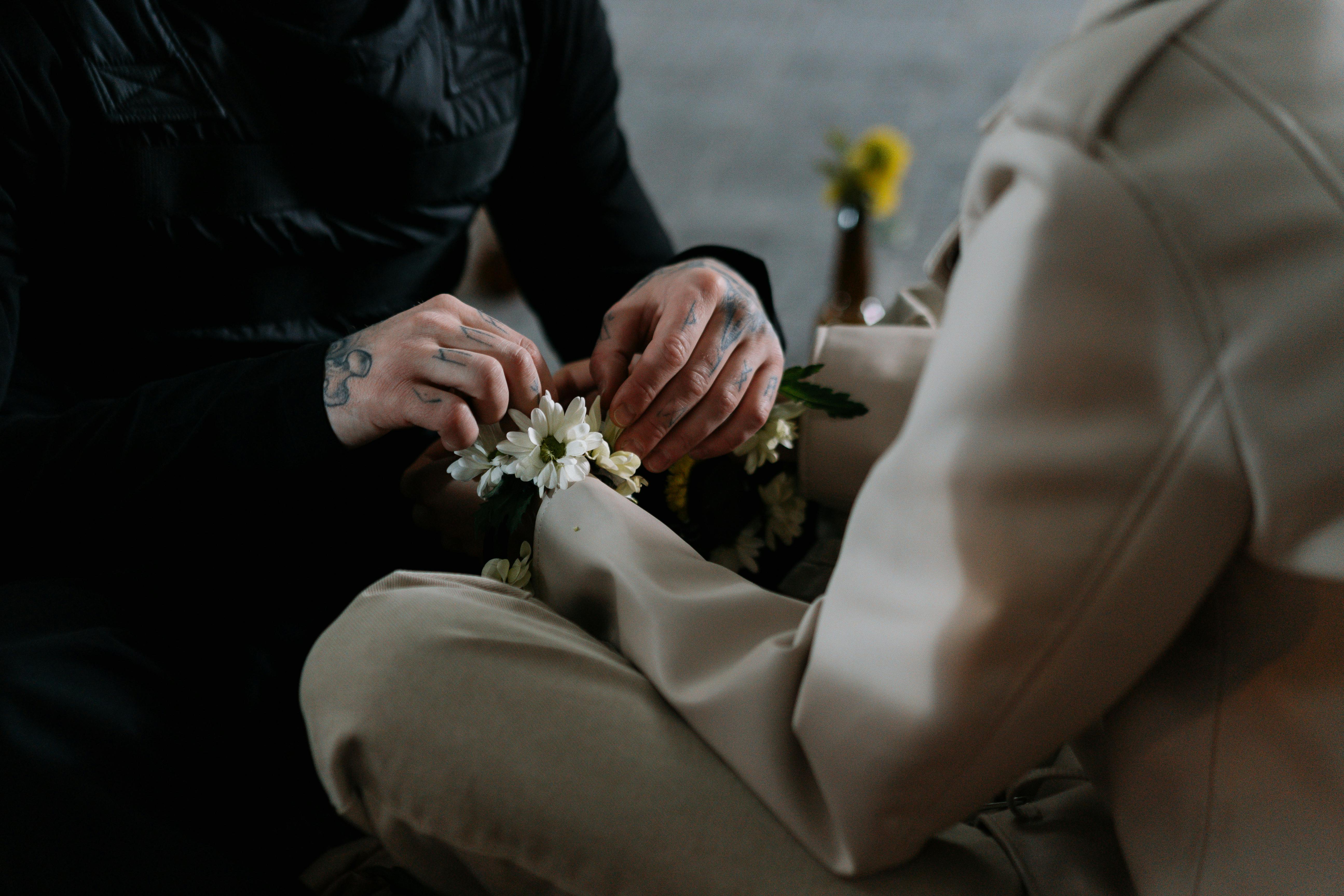 Two people making a flower crown together, hands and flowers visible.