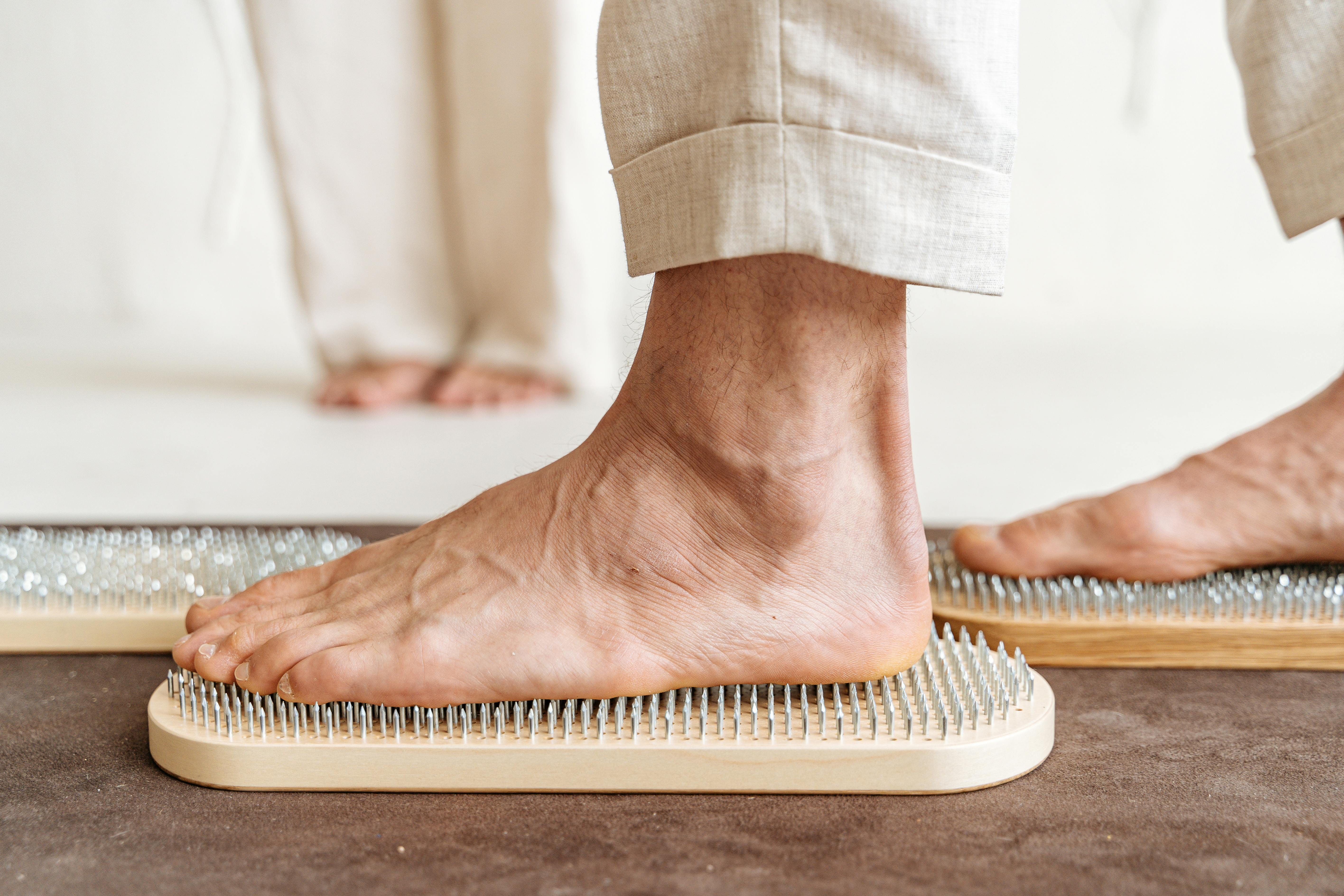 Bare feet standing on boards with metal spikes, close-up view.