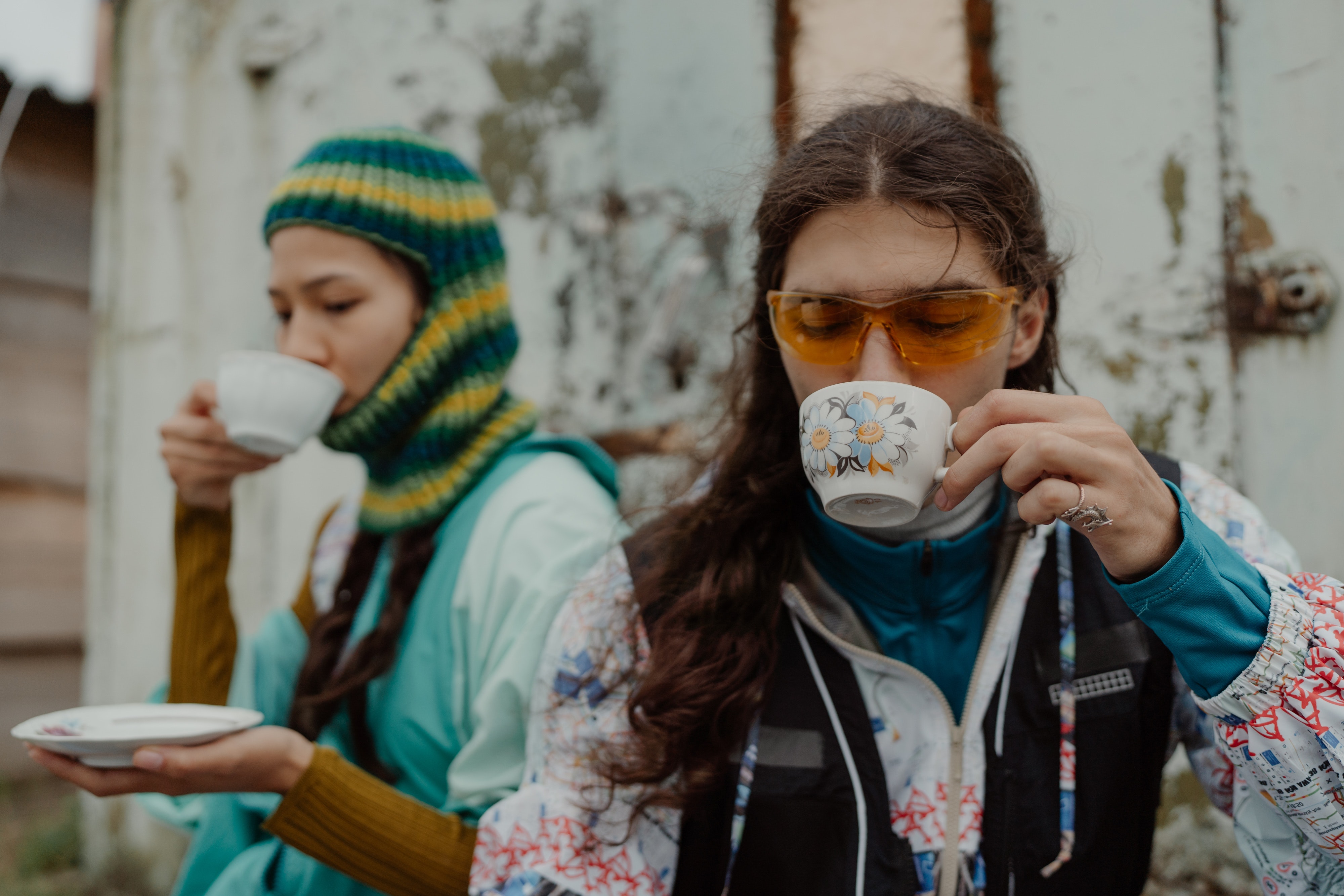 Two people outdoors, drinking tea, wearing colorful winter clothing.
