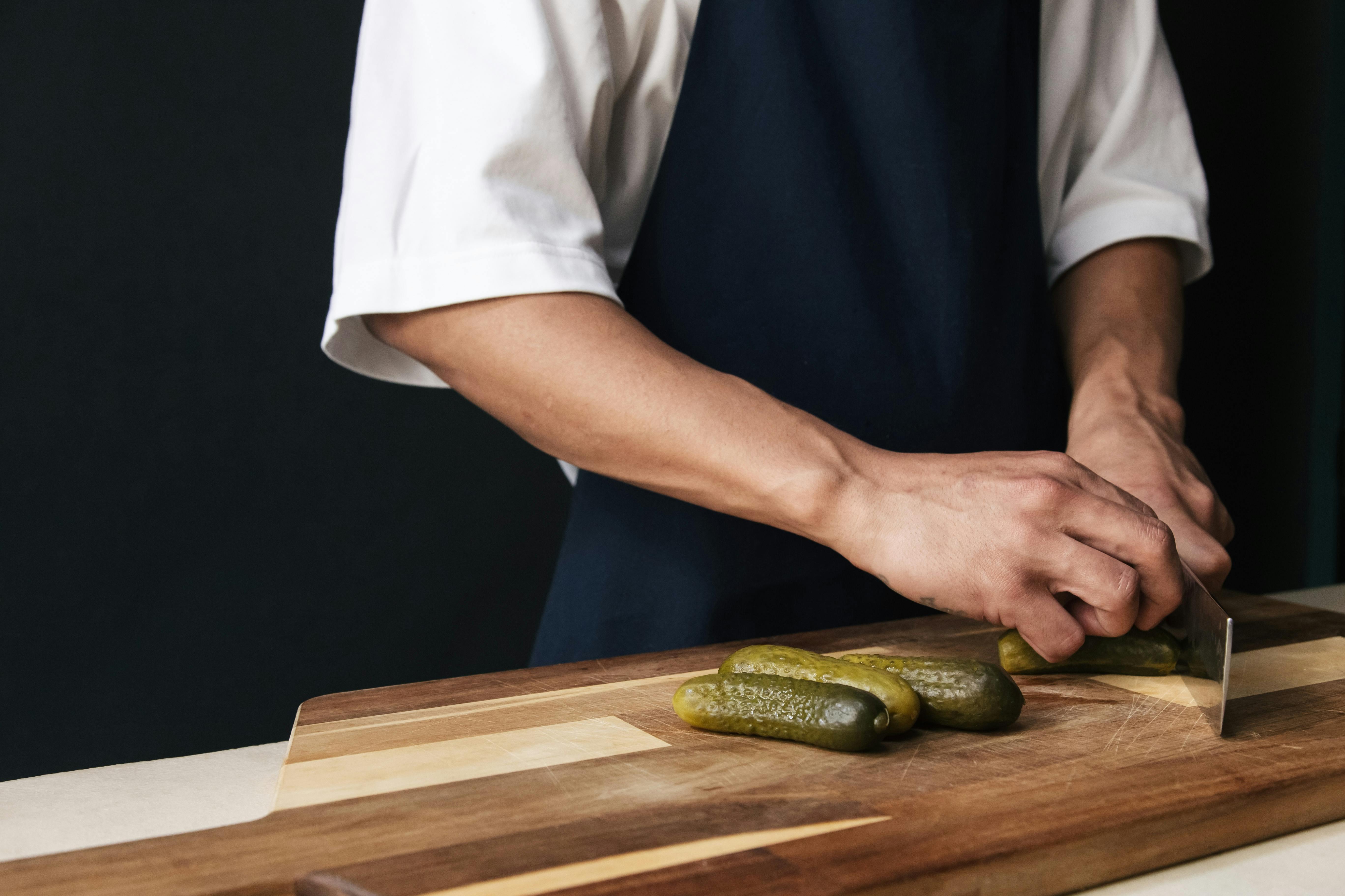 Person slicing pickles on a wooden cutting board, indoors.