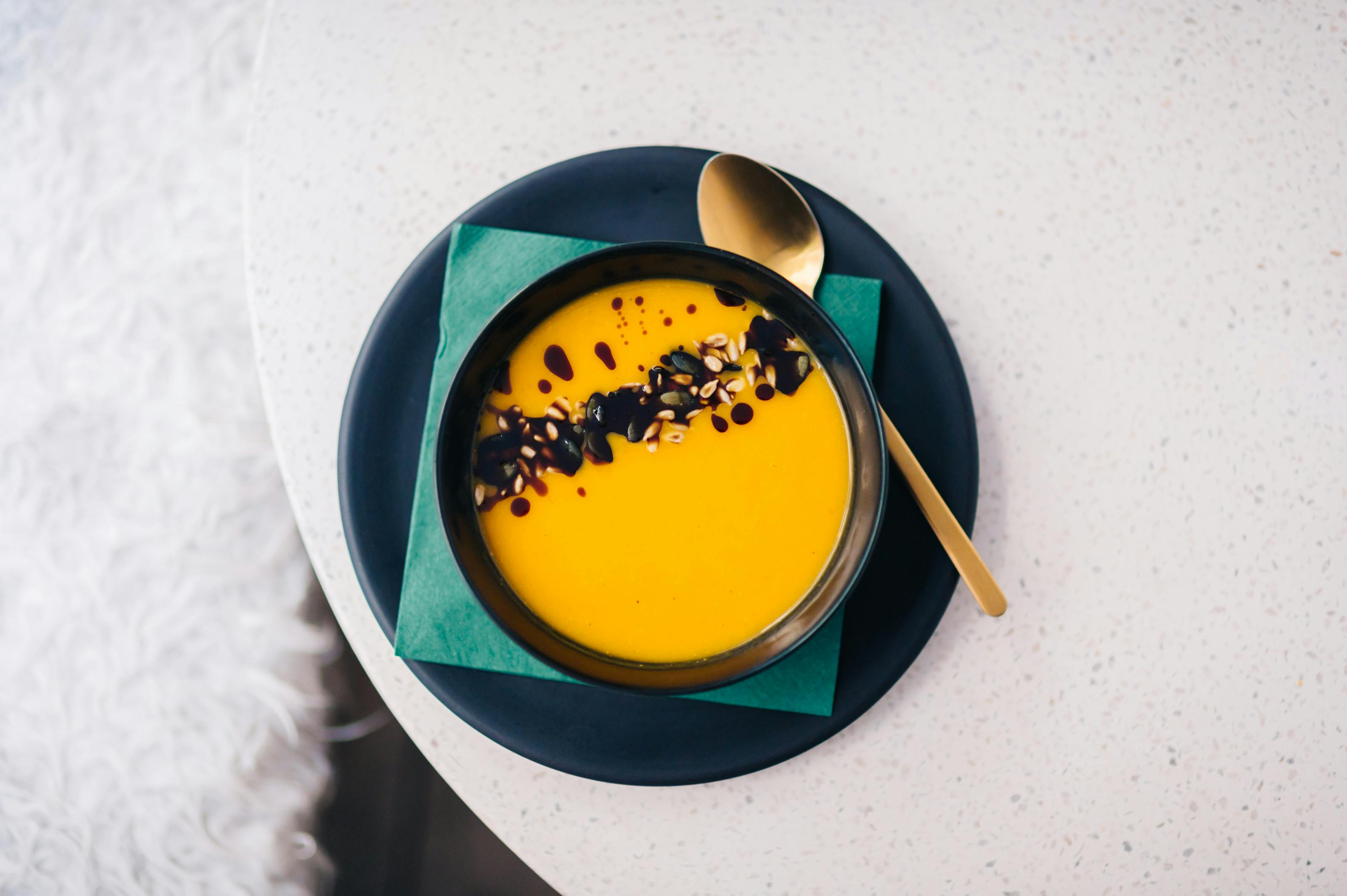 Bowl of orange soup with seeds, spoon, and napkin.