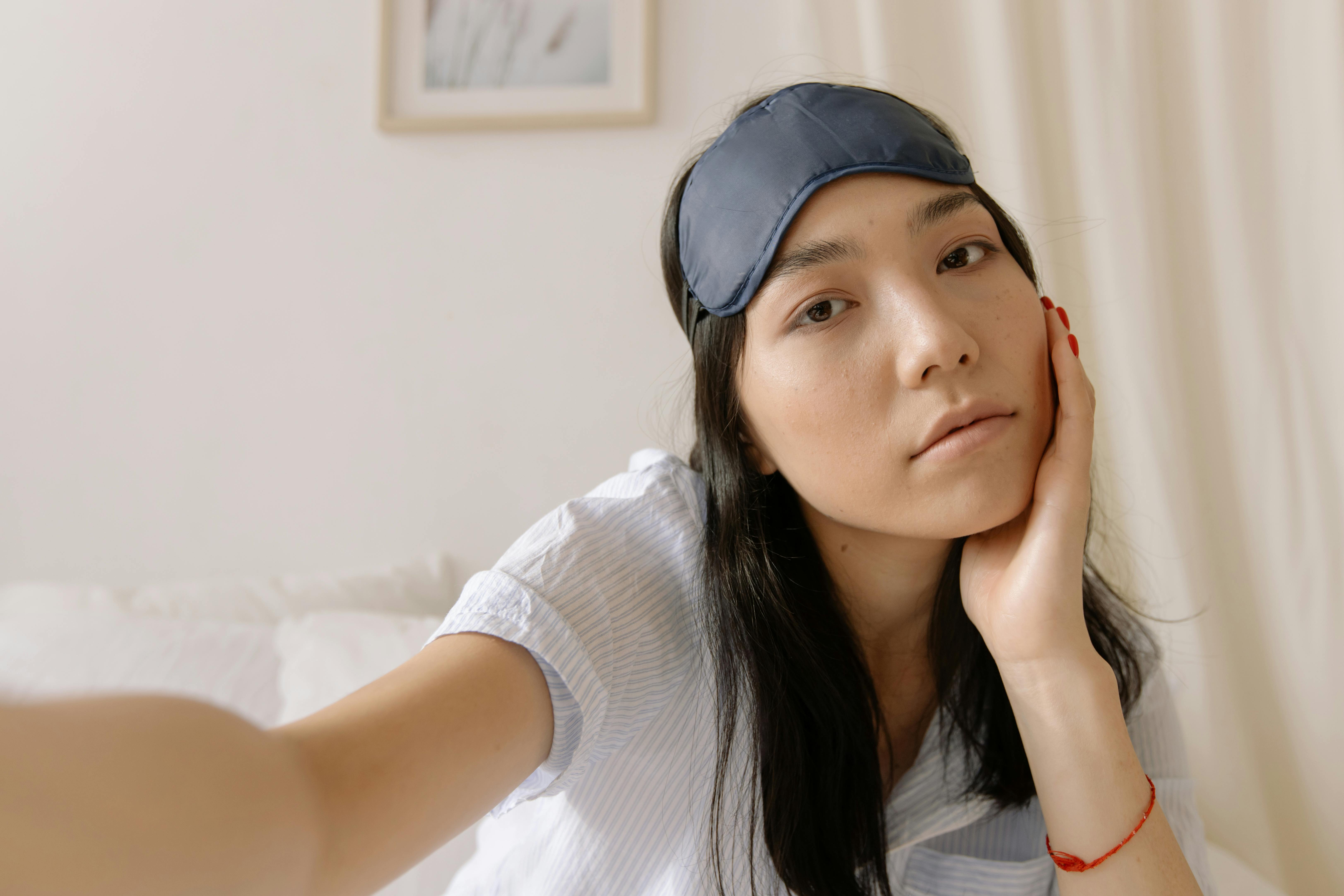 Person with sleep mask on head, sitting on bed, relaxed.