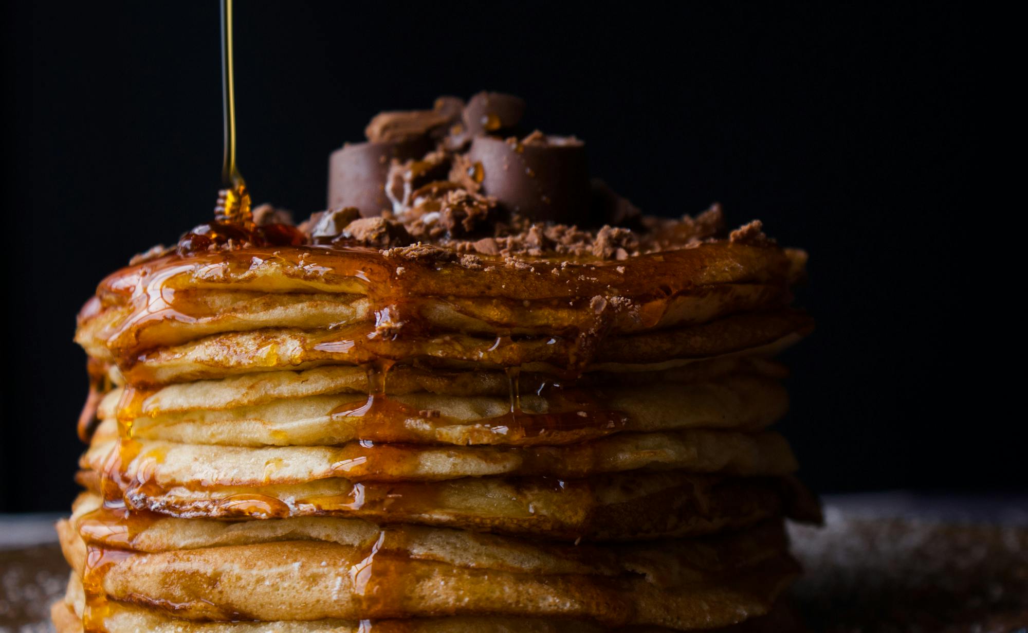 Stack of pancakes with syrup and chocolate, dark background.