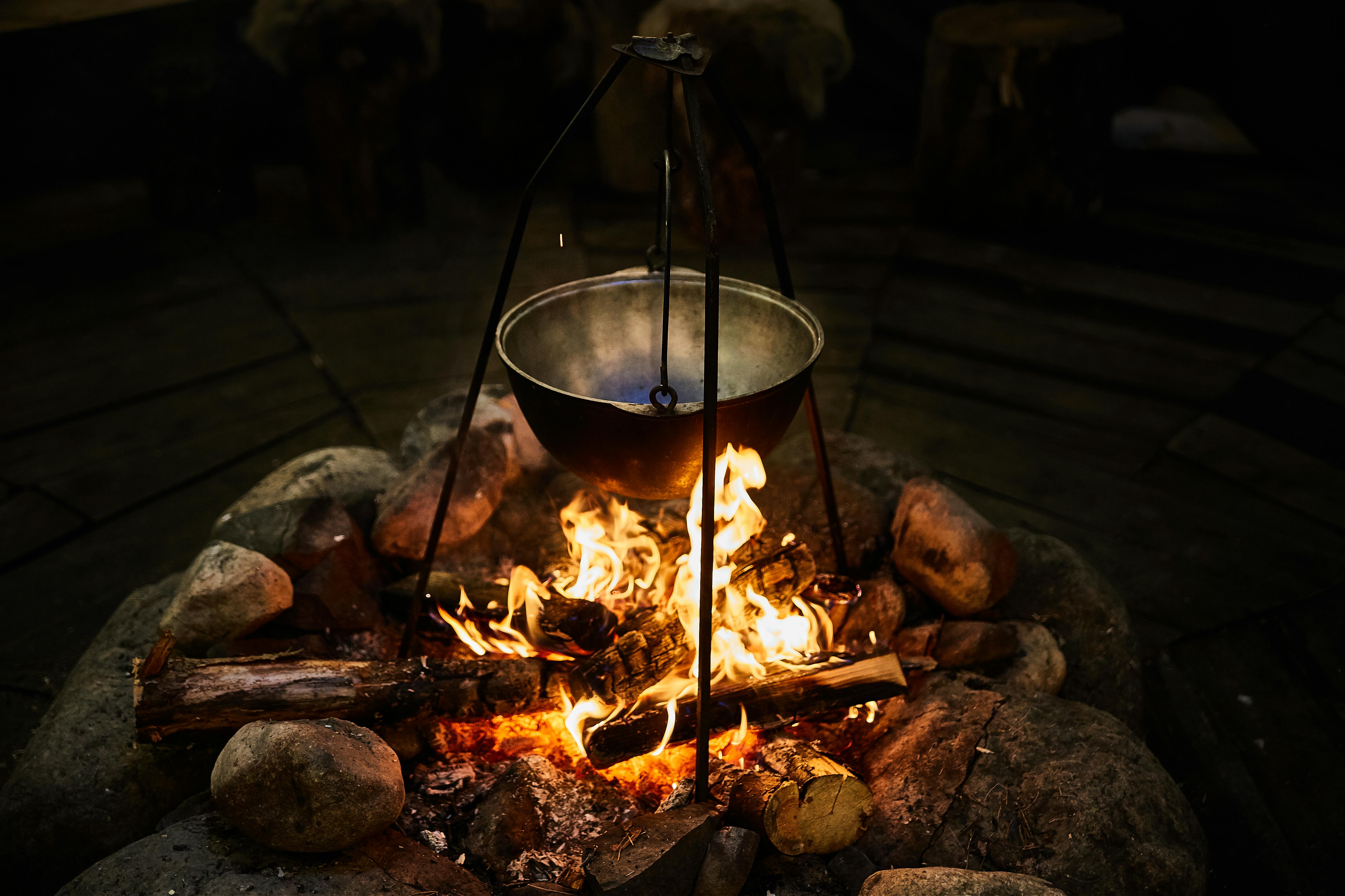 Metal pot hanging over campfire, surrounded by rocks and logs.