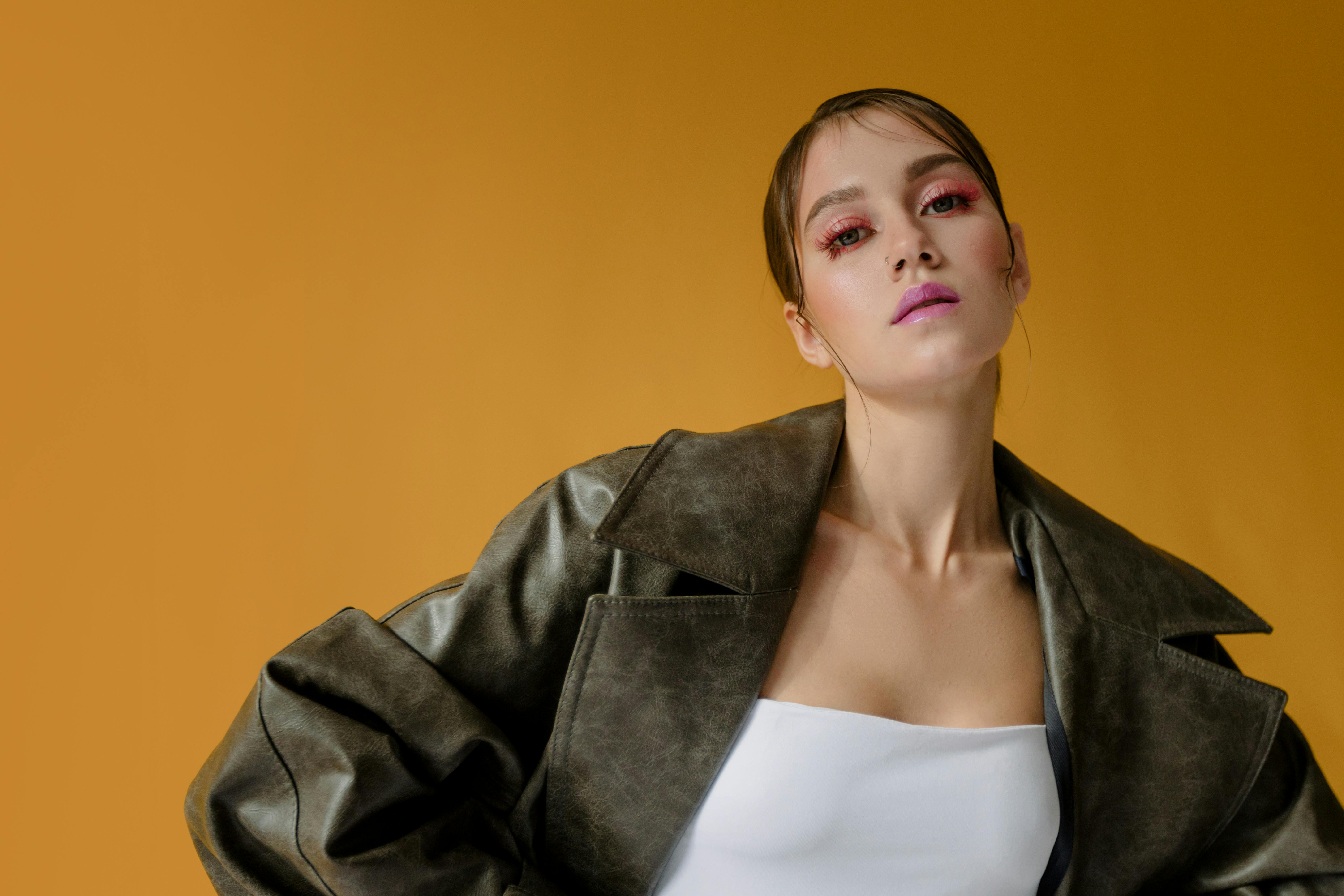 Person in stylish jacket poses against solid yellow background, confident.