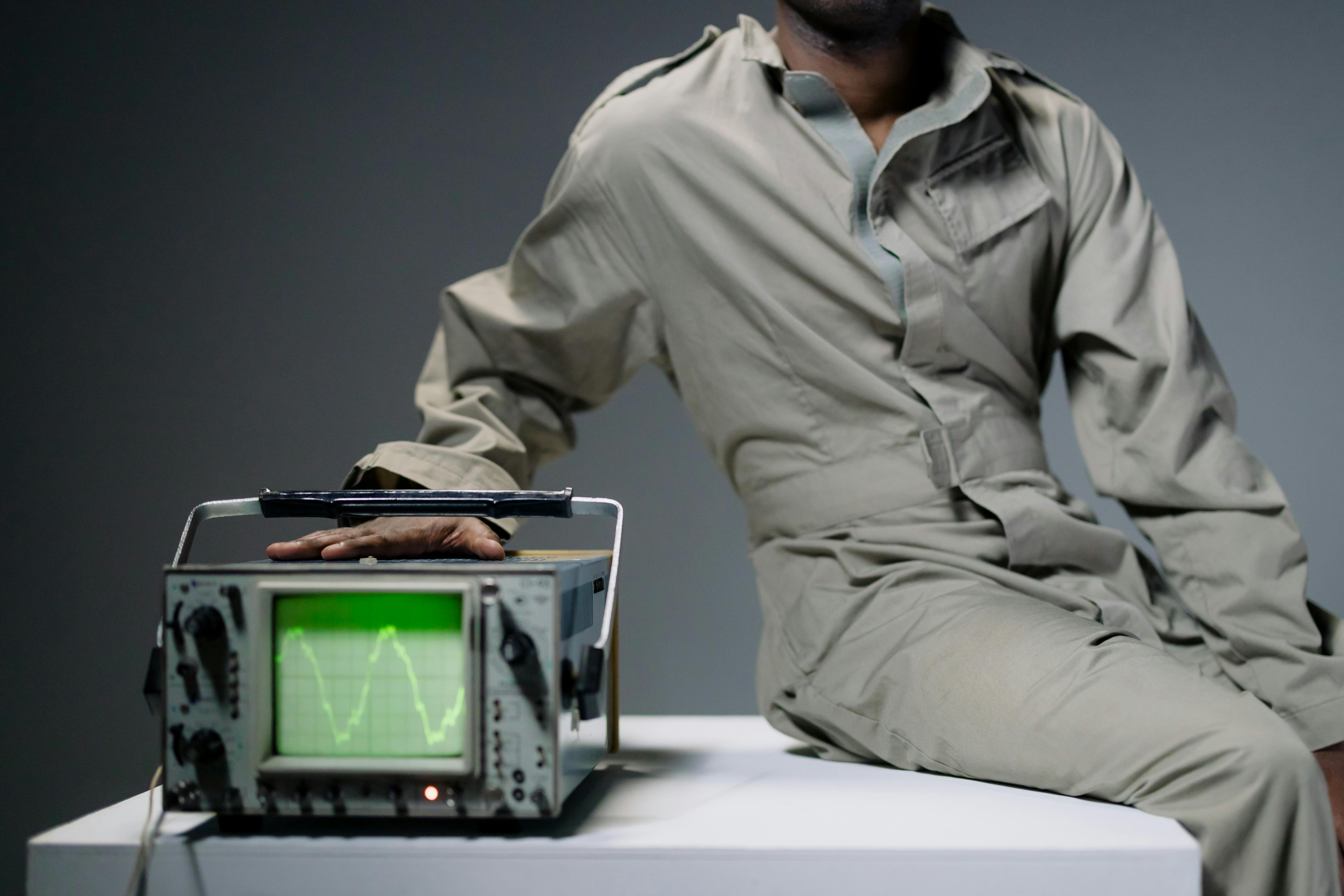 Person in jumpsuit with hand on oscilloscope displaying waveform.