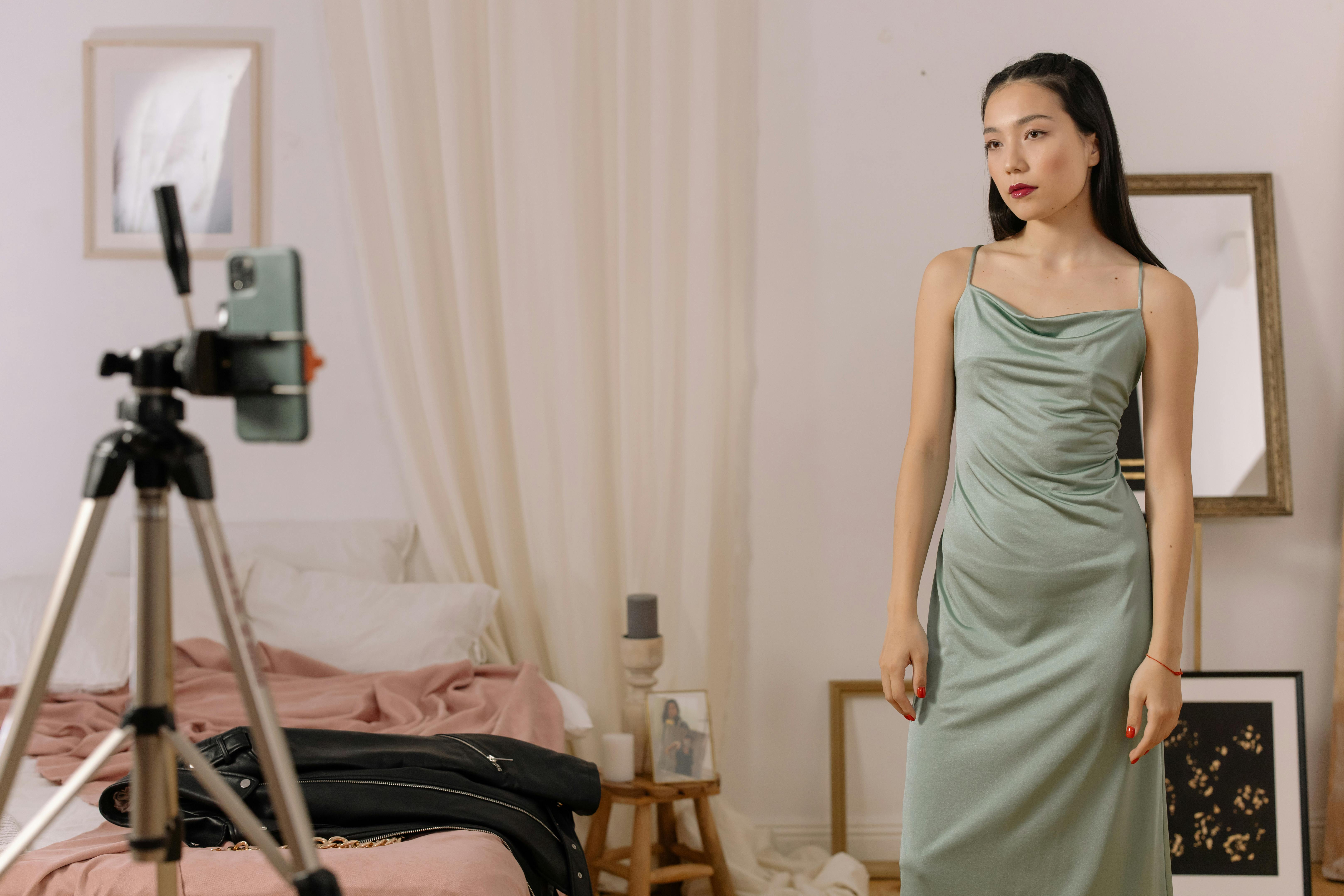 Person in green dress posing for camera in bedroom setting.