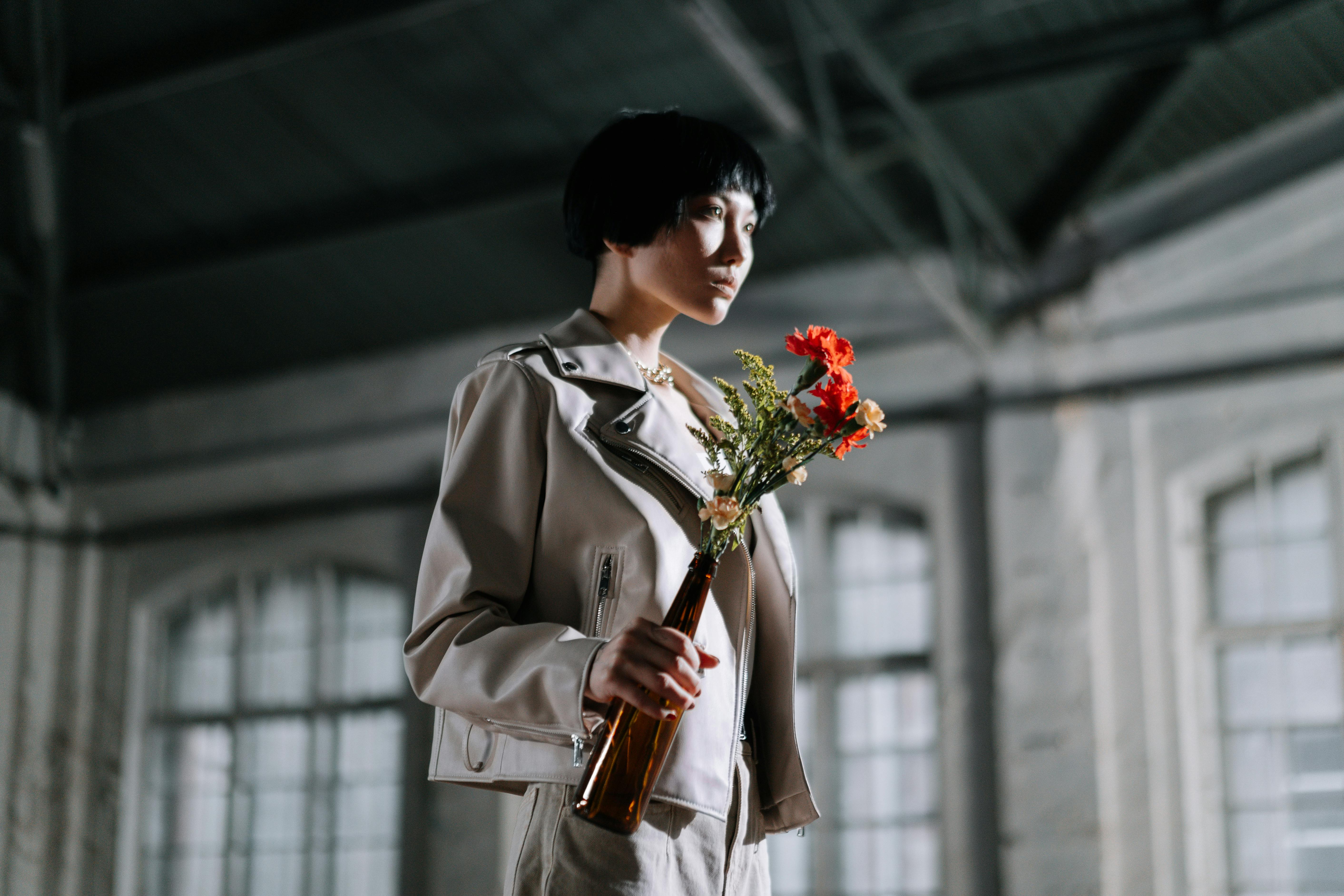 Person in light jacket holding flowers in a brown bottle.