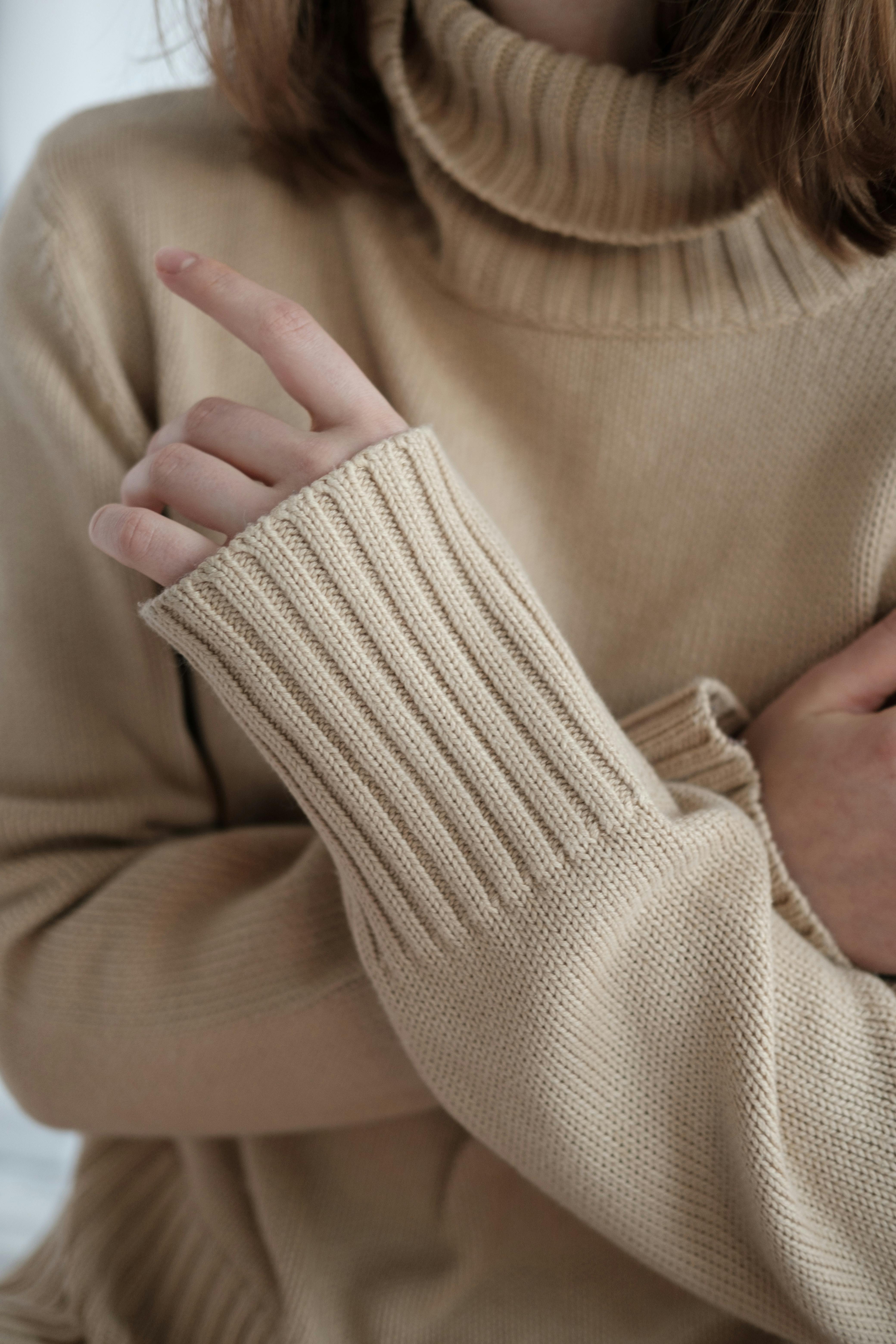 Person wearing beige turtleneck sweater, hand partially raised, cozy atmosphere.