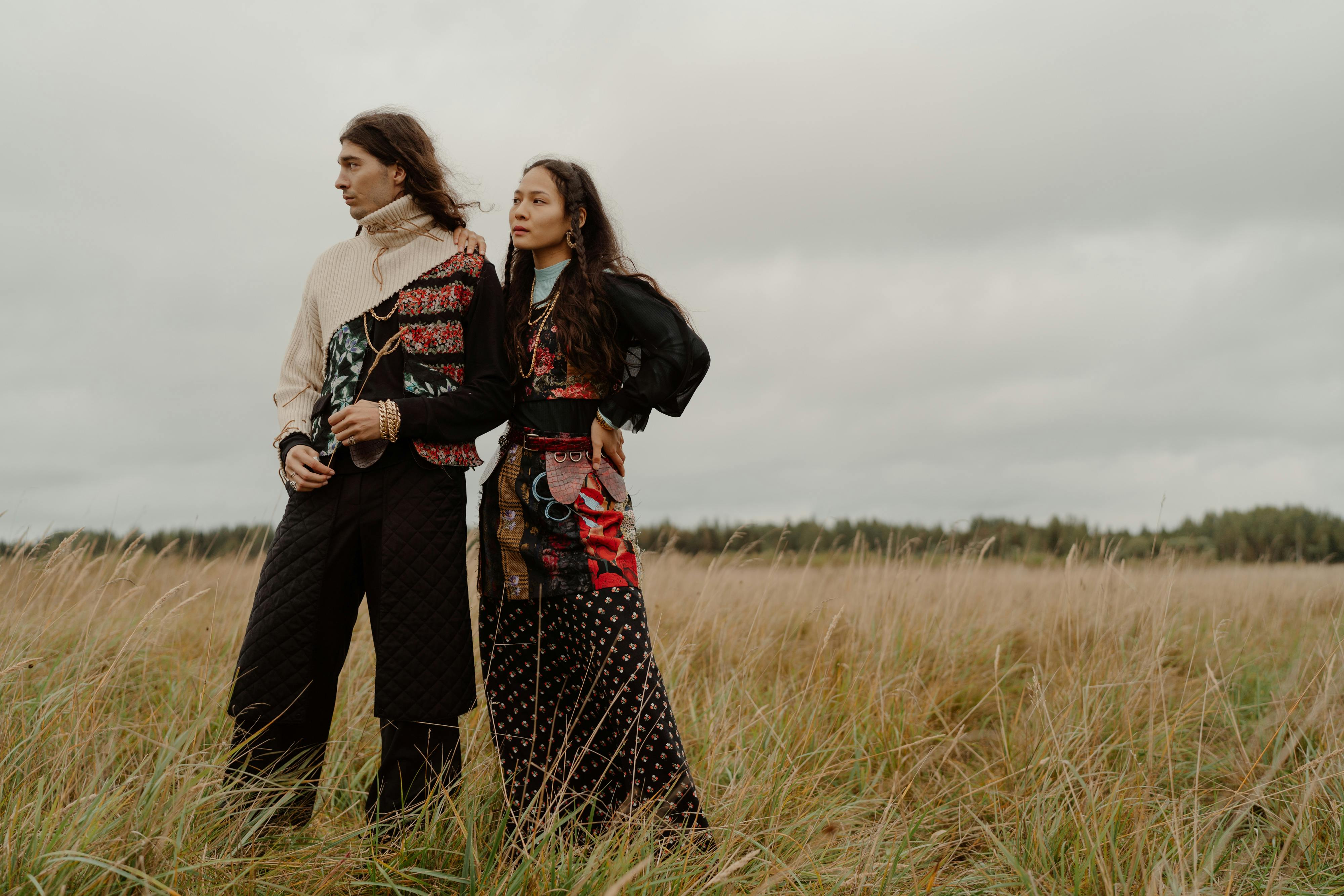 Two people stand in a field of tall grass under a cloudy sky.