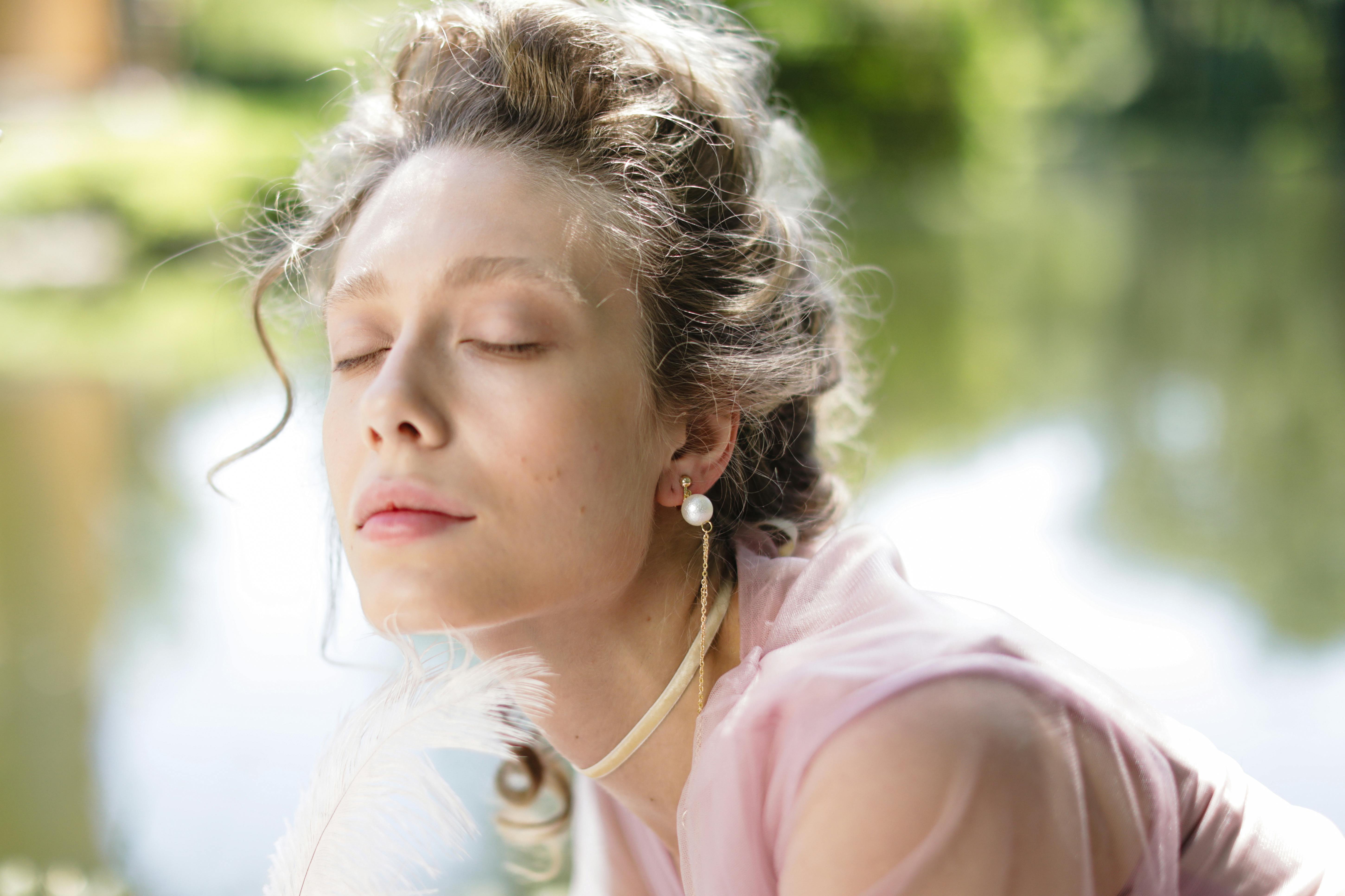 A person with eyes closed, wearing a pearl earring and pink dress.