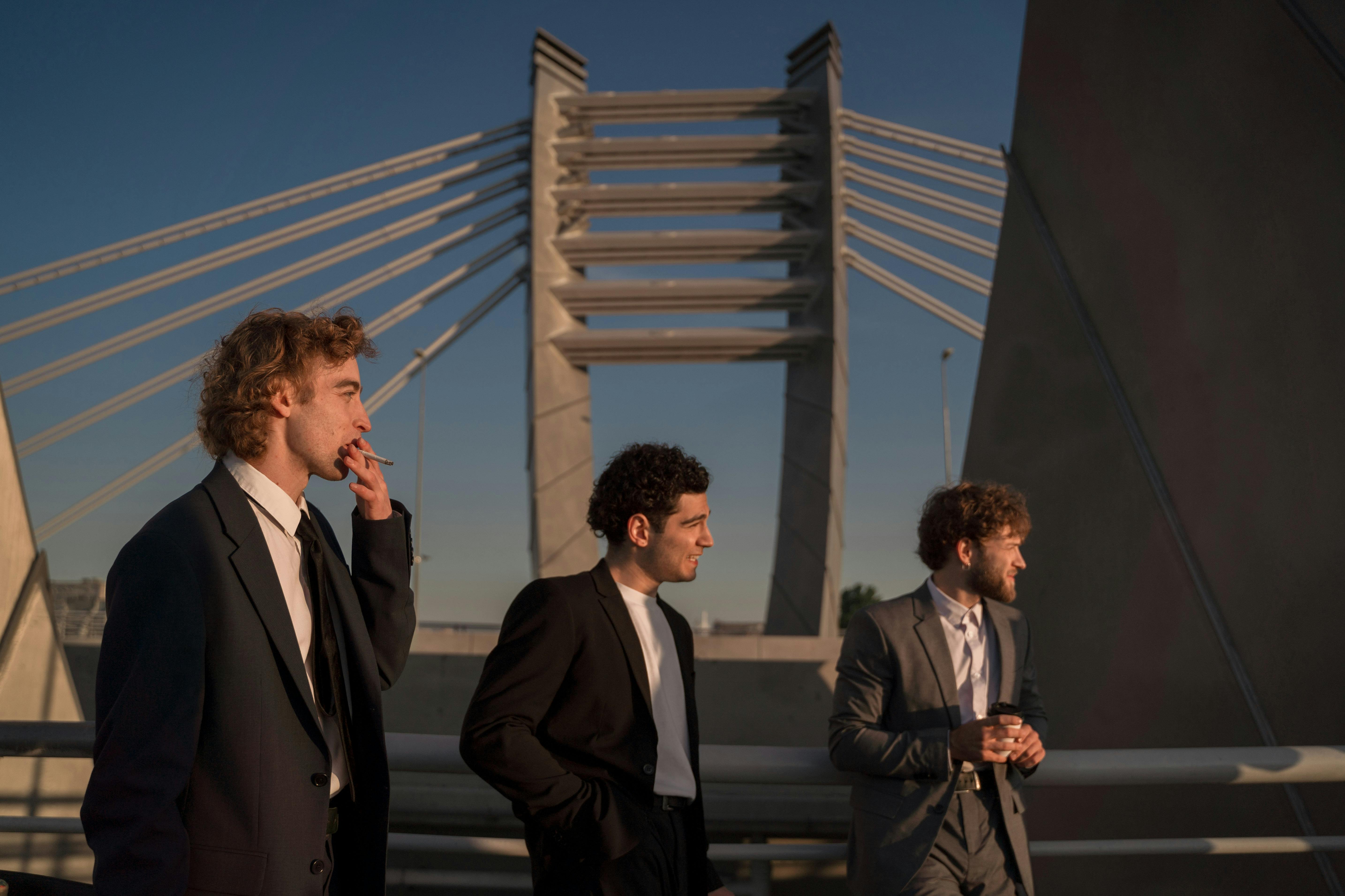Three men in suits stand on a bridge with a modern architectural design.