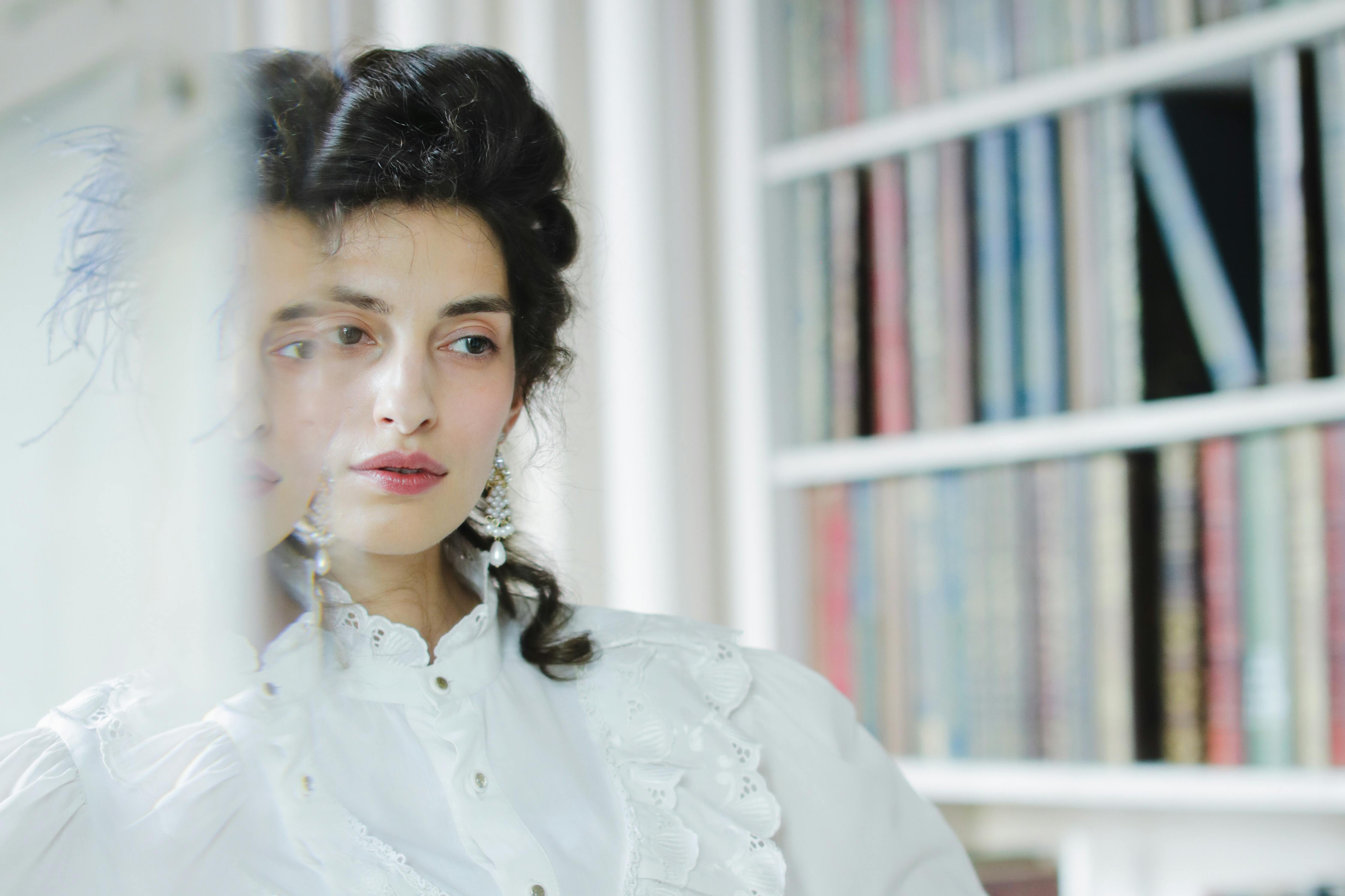 A person in a white ruffled shirt looks into a mirror.