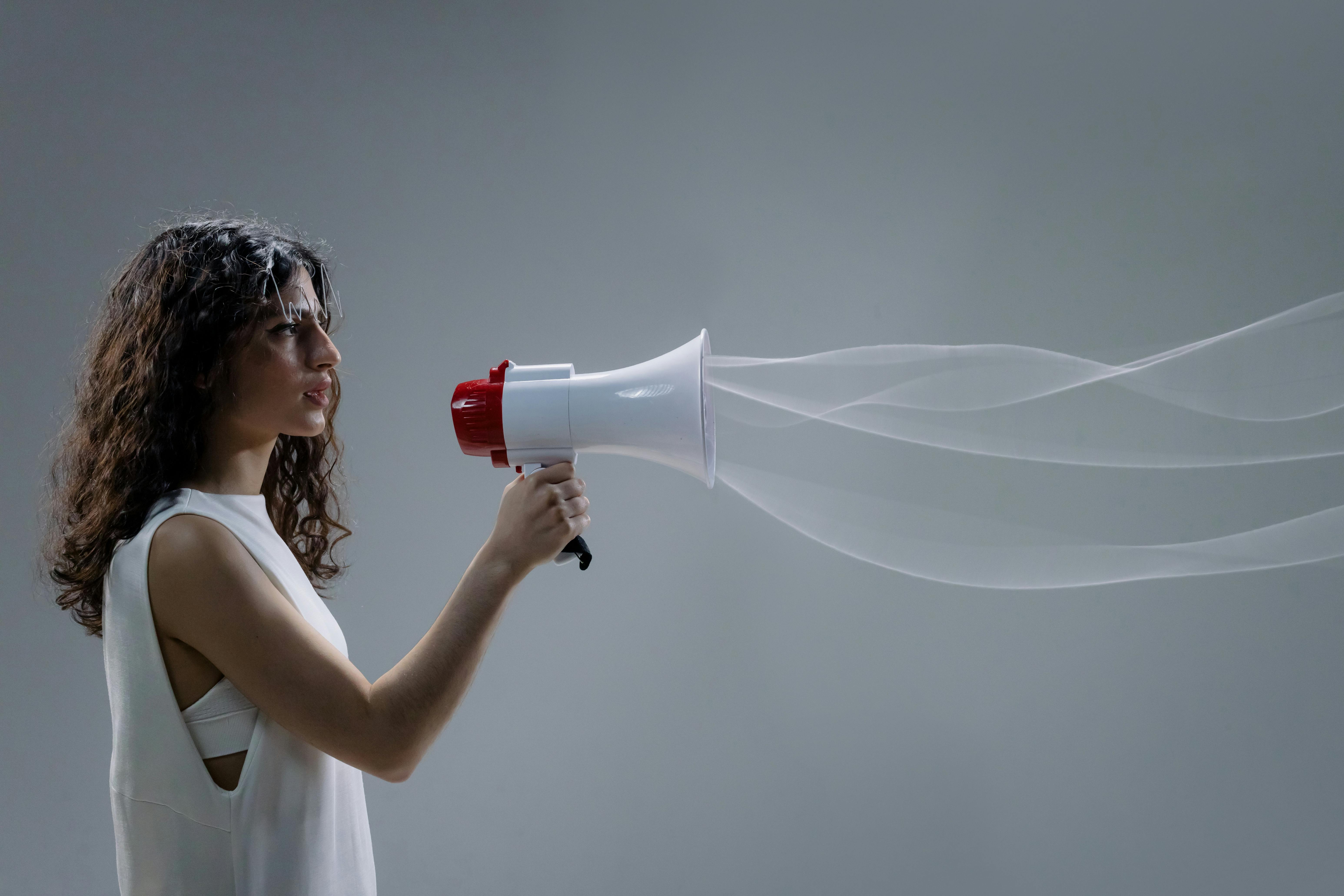 Person holding megaphone, sound waves illustrated, gray background, indoors.