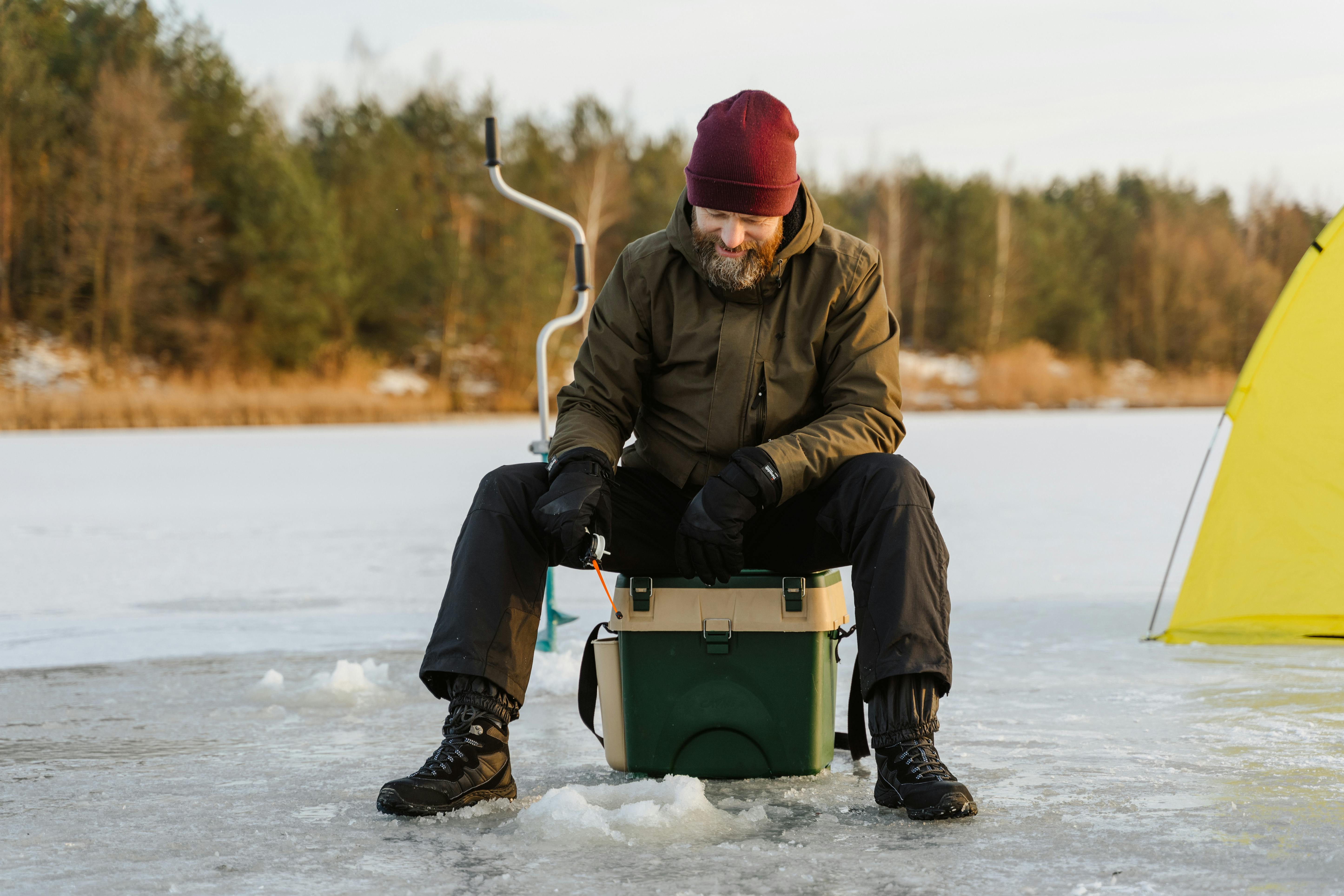 Person ice fishing on a frozen lake with a yellow tent.