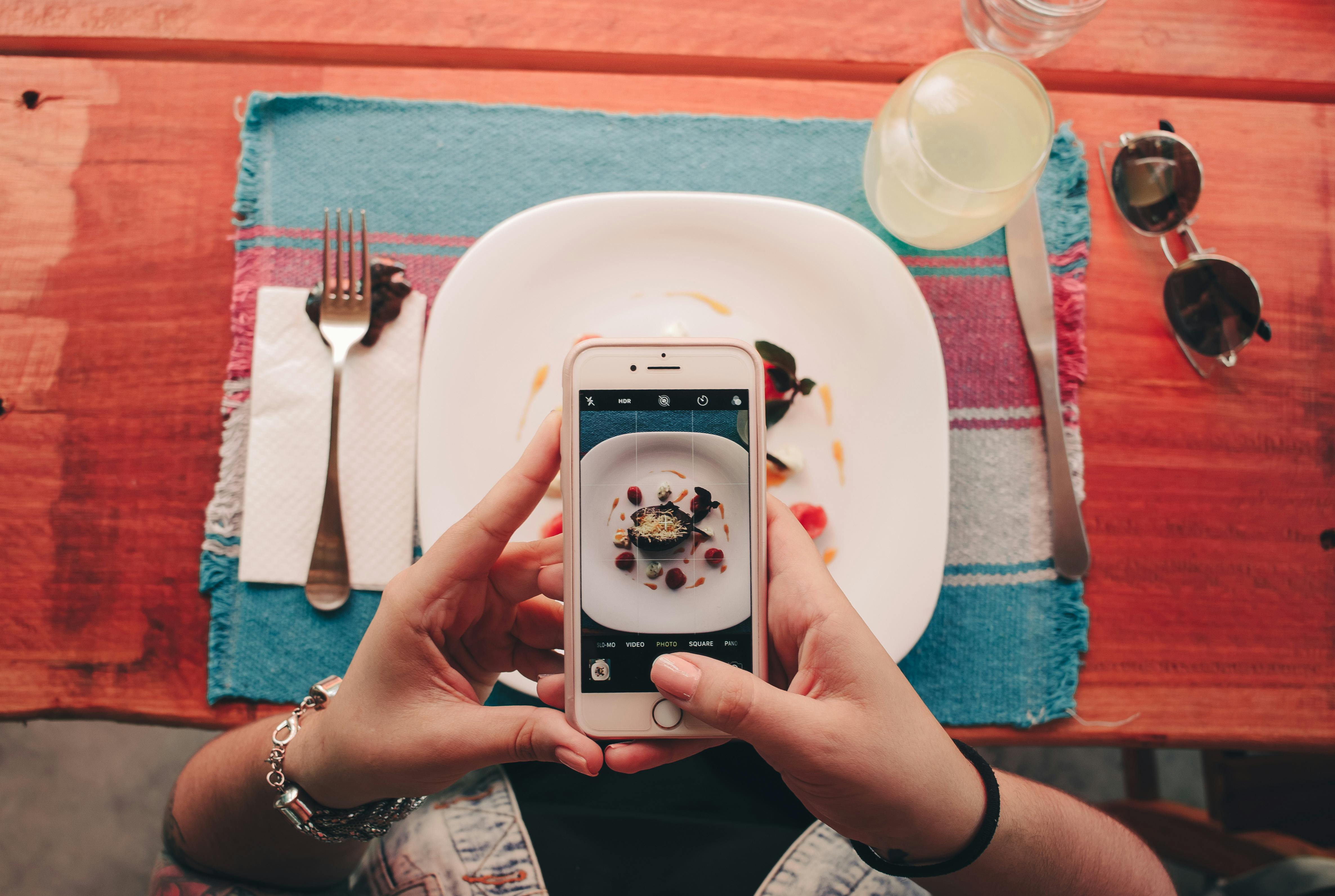 Person taking a photo of food with a smartphone at table.