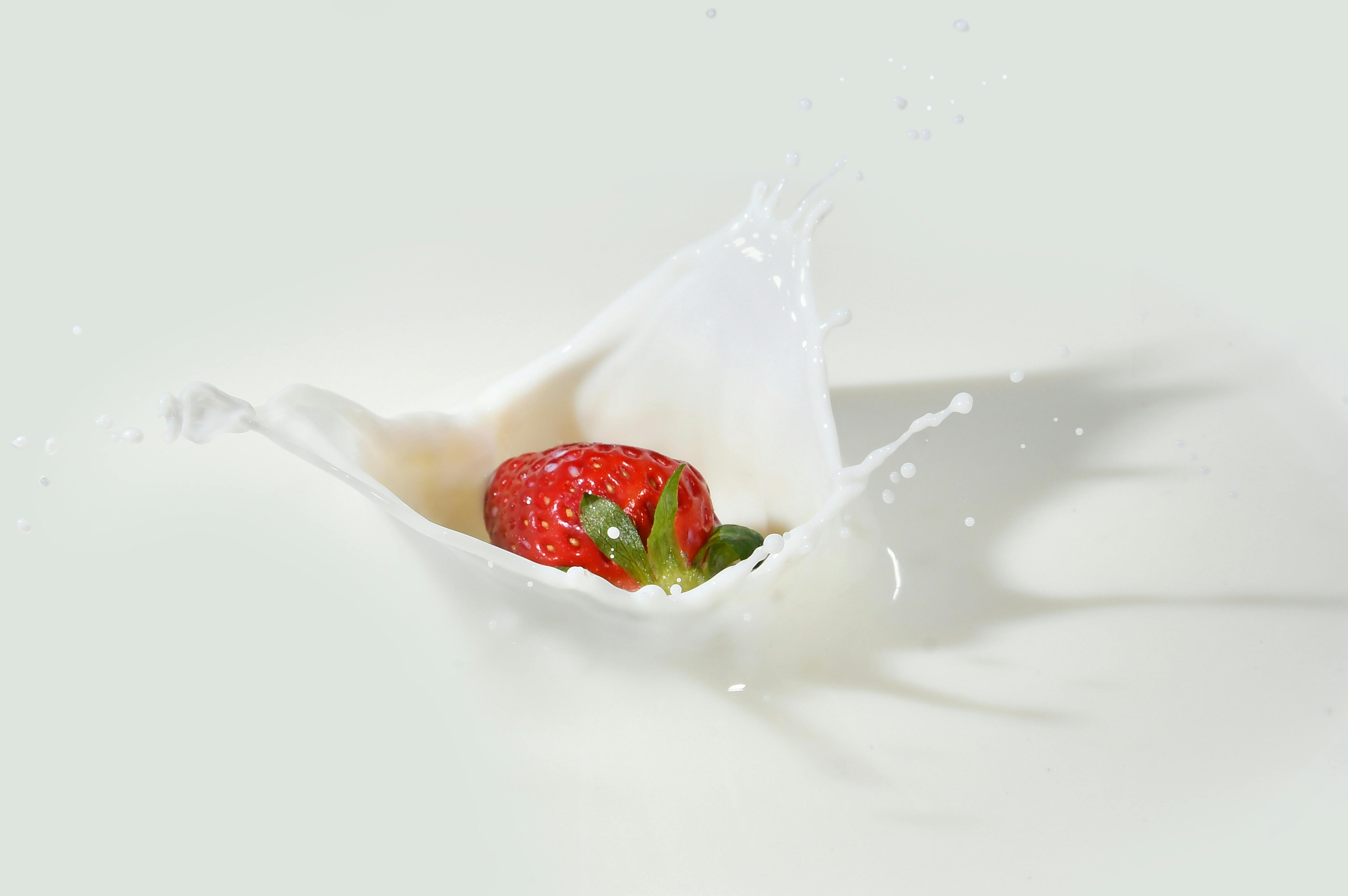A strawberry splashes into milk, creating a dramatic white splash.