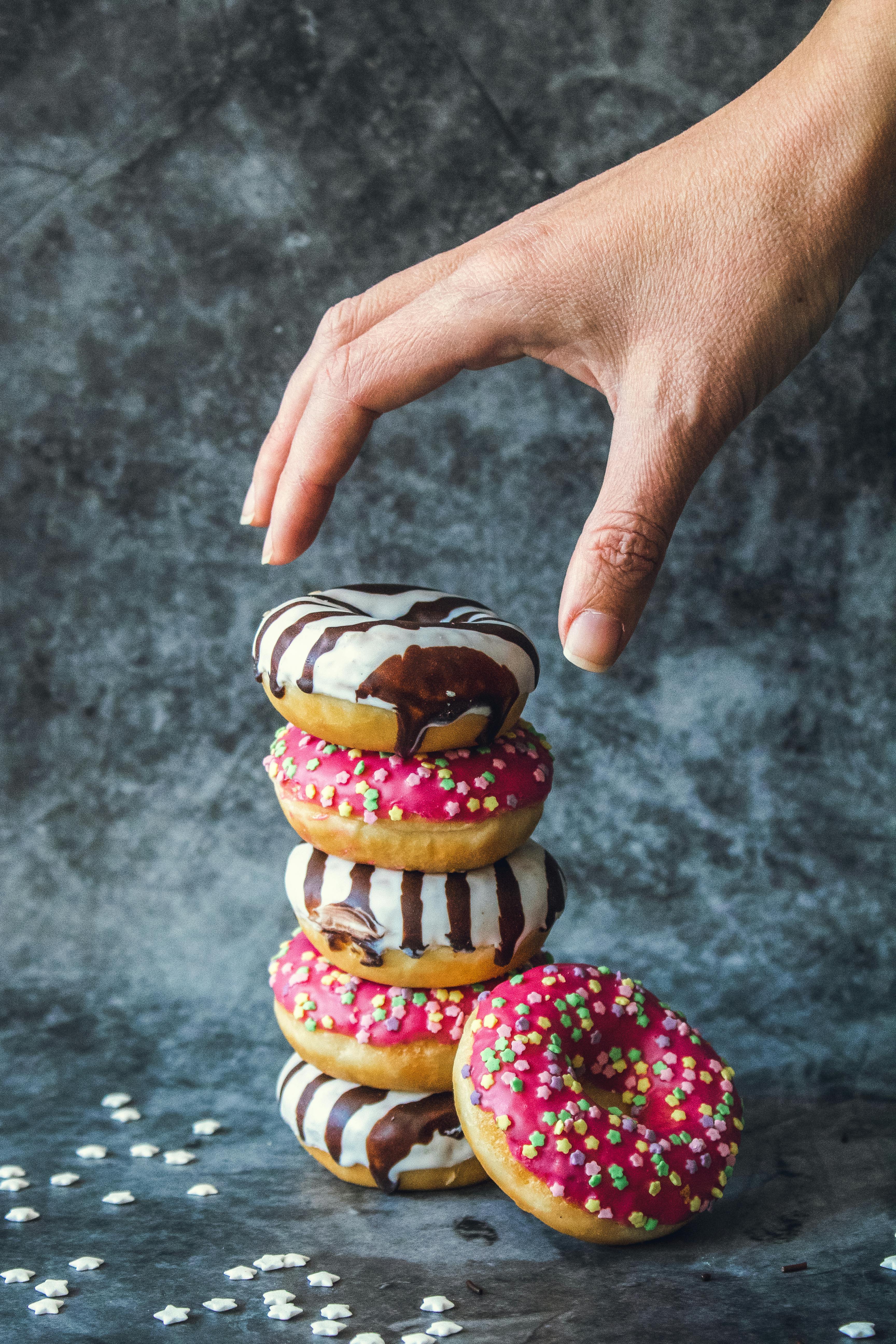 Hand reaching for stacked donuts with colorful icing and sprinkles.