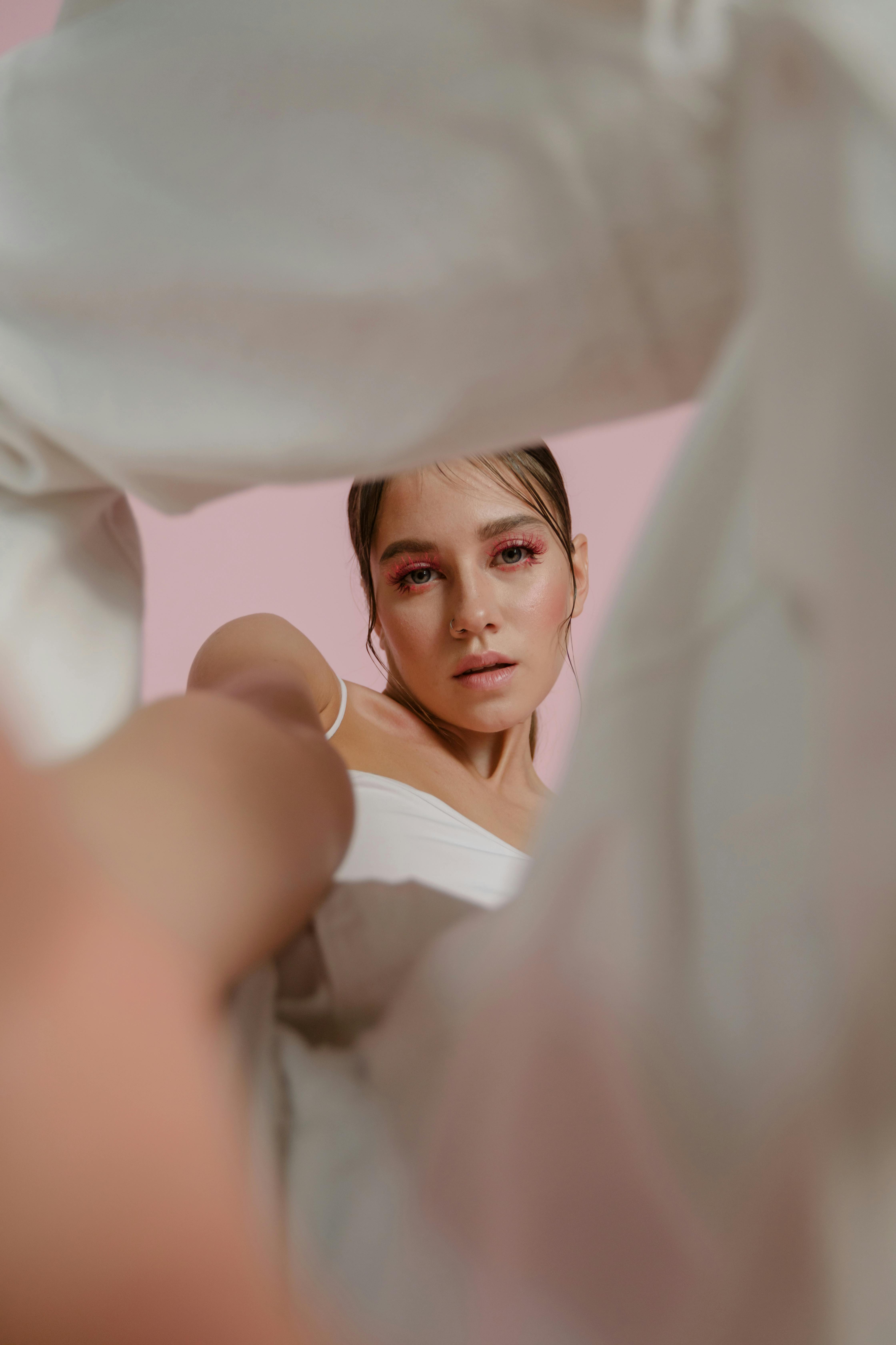 Person with pink makeup framed by white fabric, pink background.