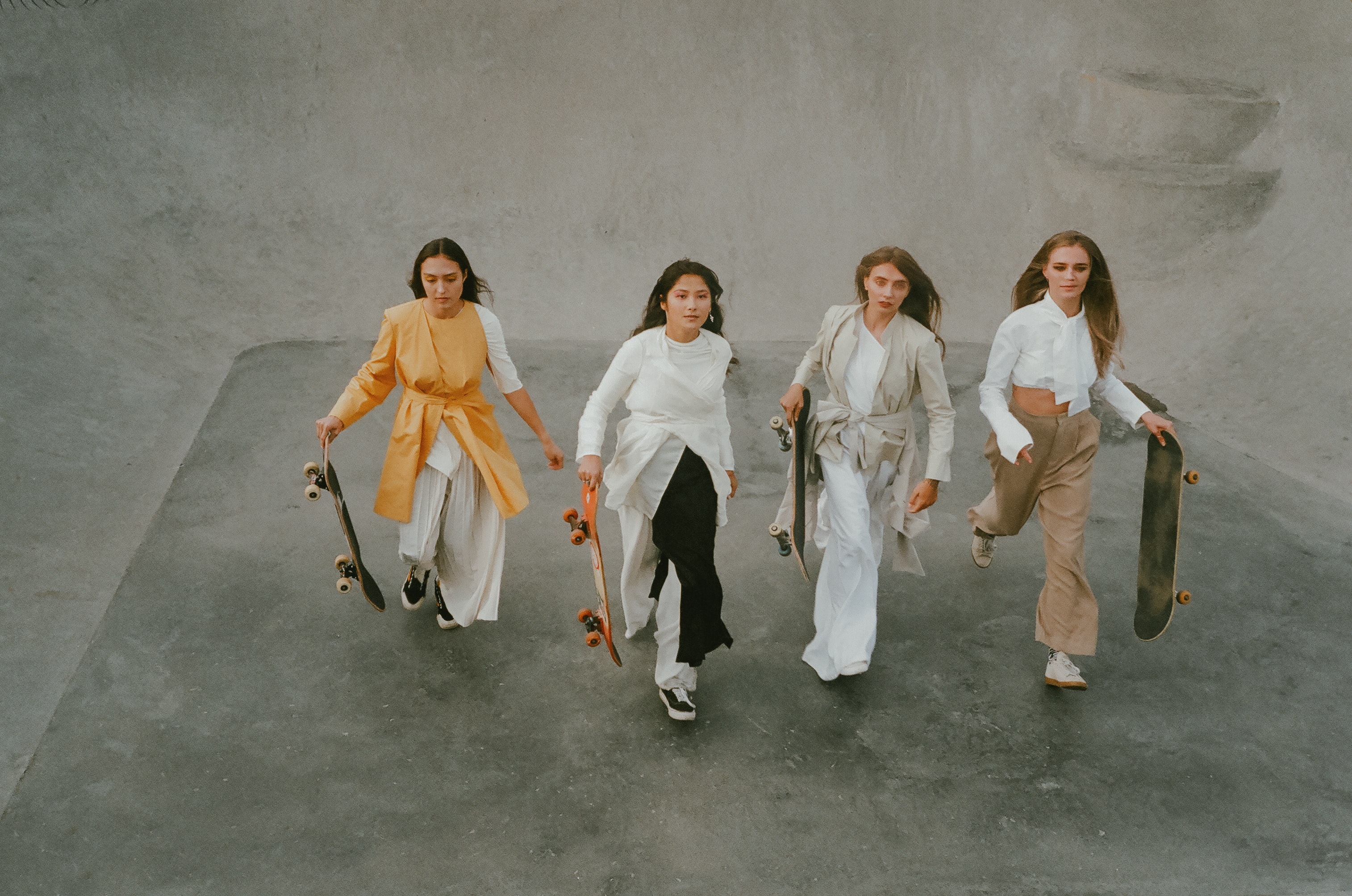 Four people walking with skateboards in a concrete skatepark.