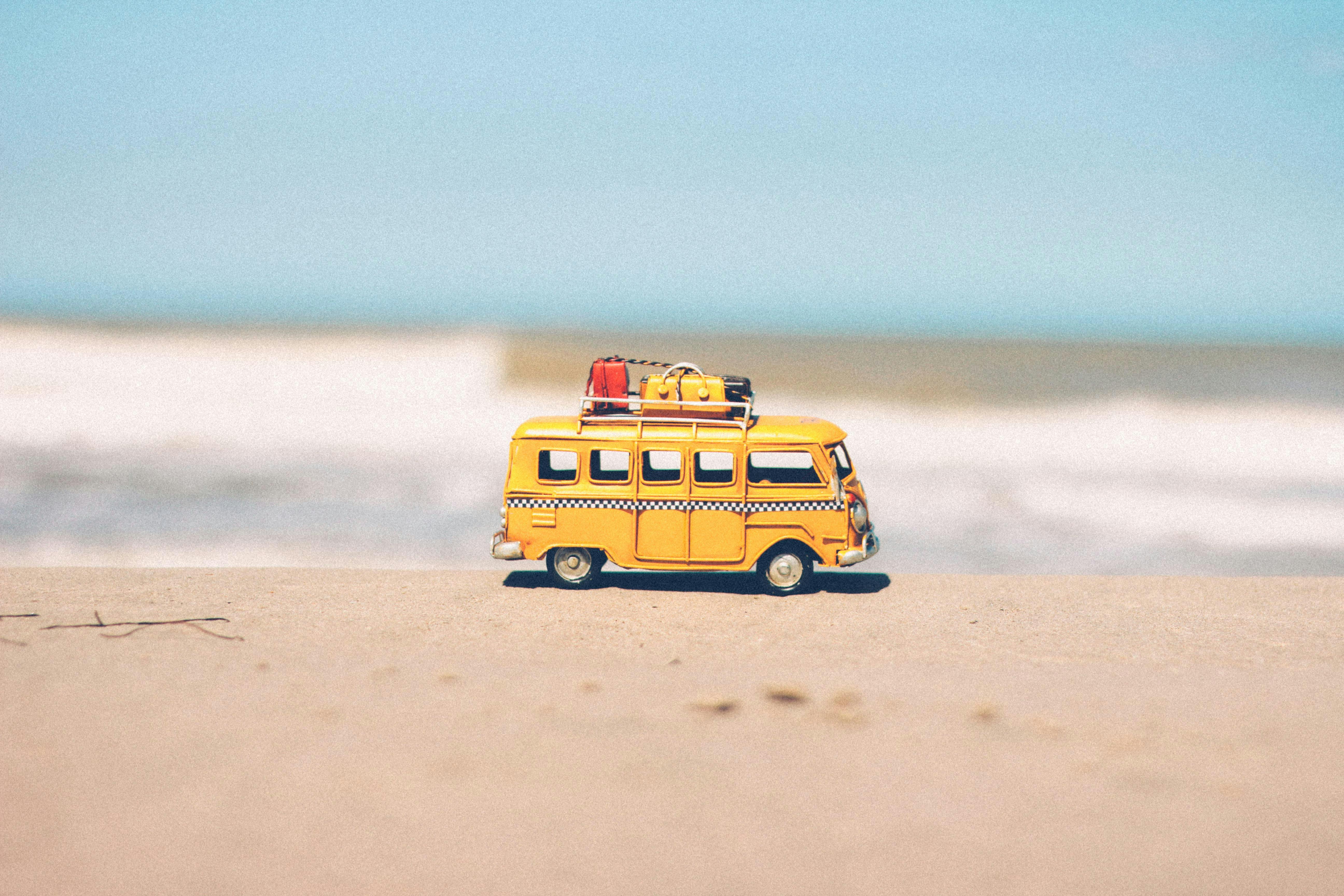 Toy yellow van with luggage on sandy beach, blue sky.