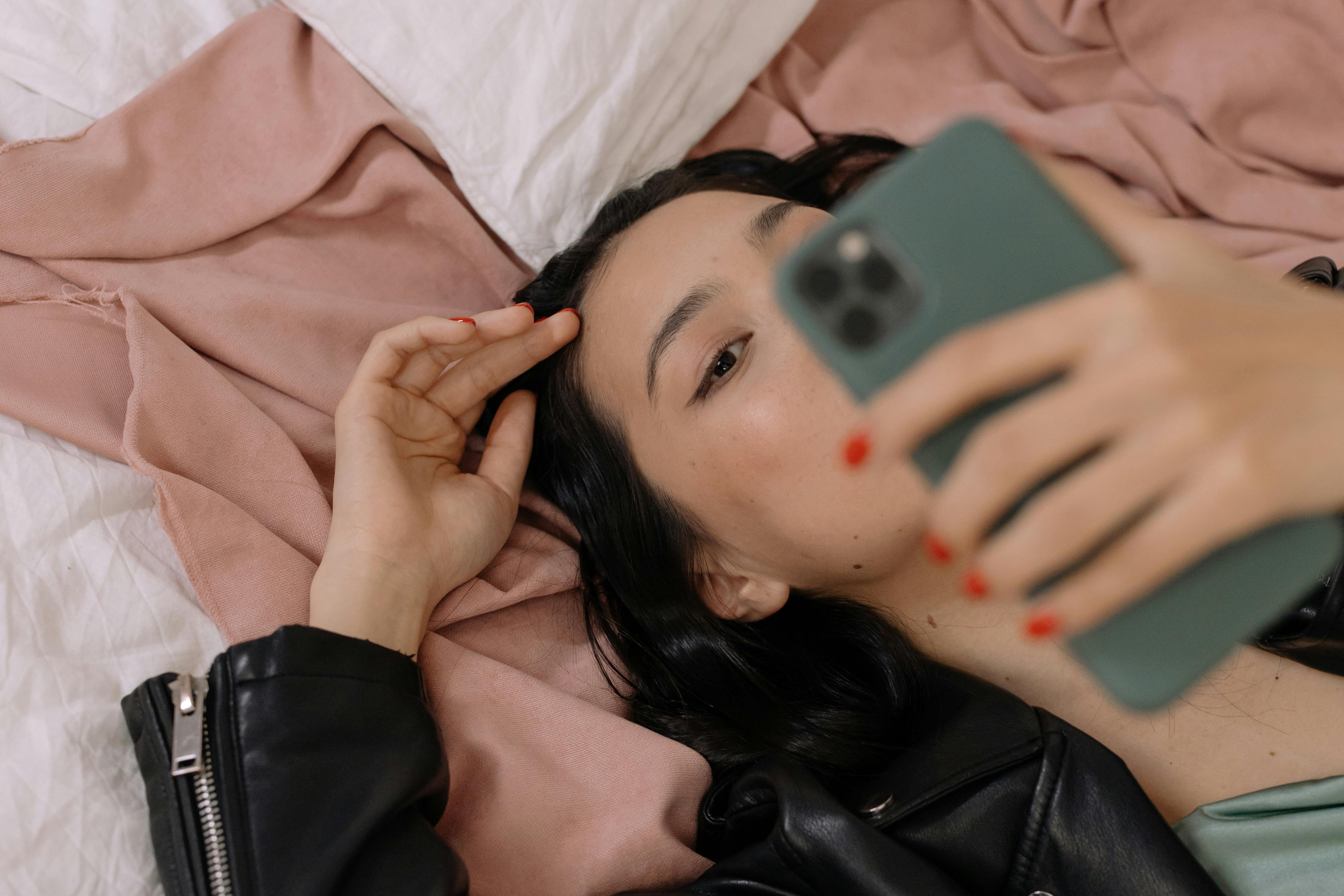Person lying on bed, holding phone, taking a selfie.