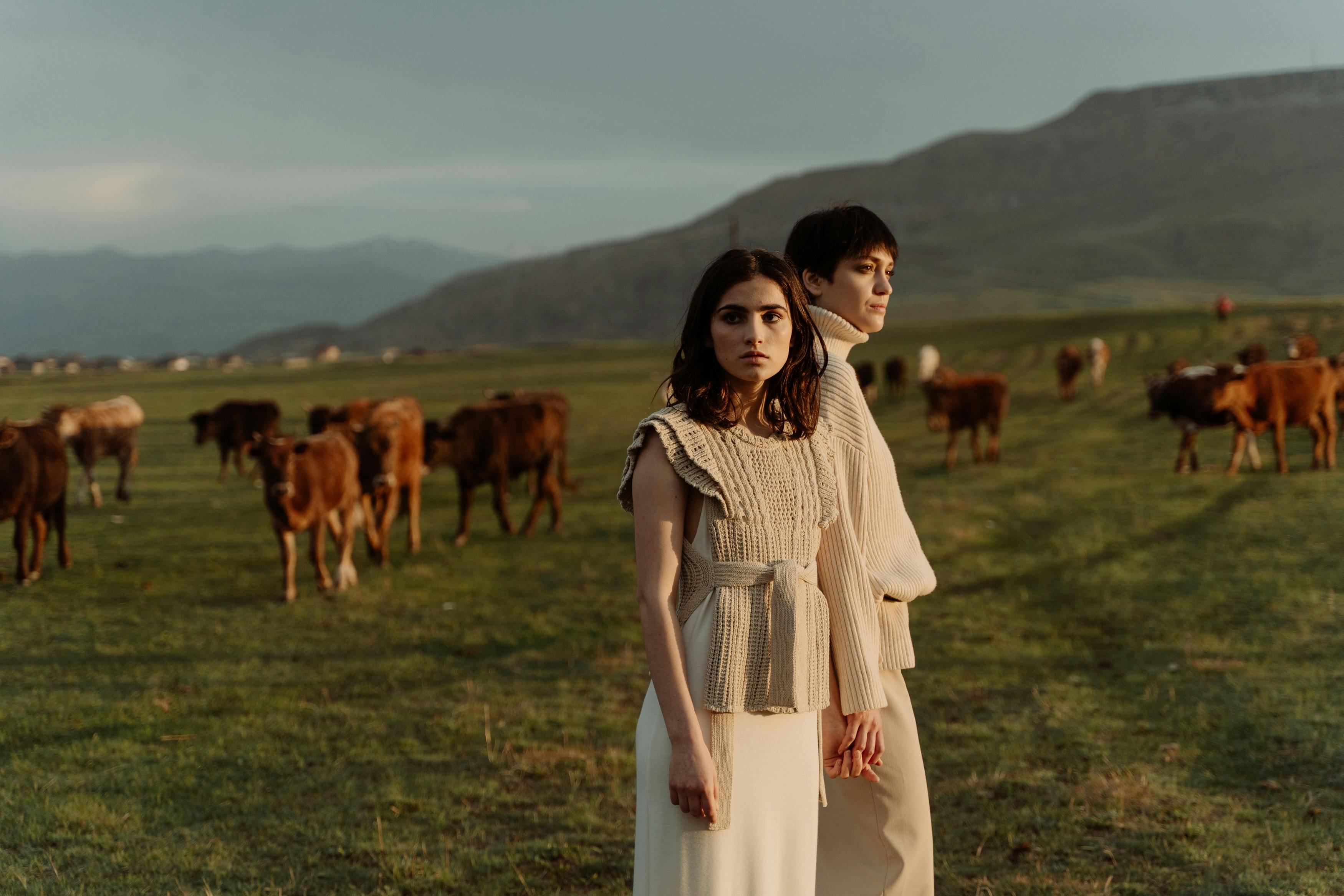 Two people stand in a field with cows and mountains.
