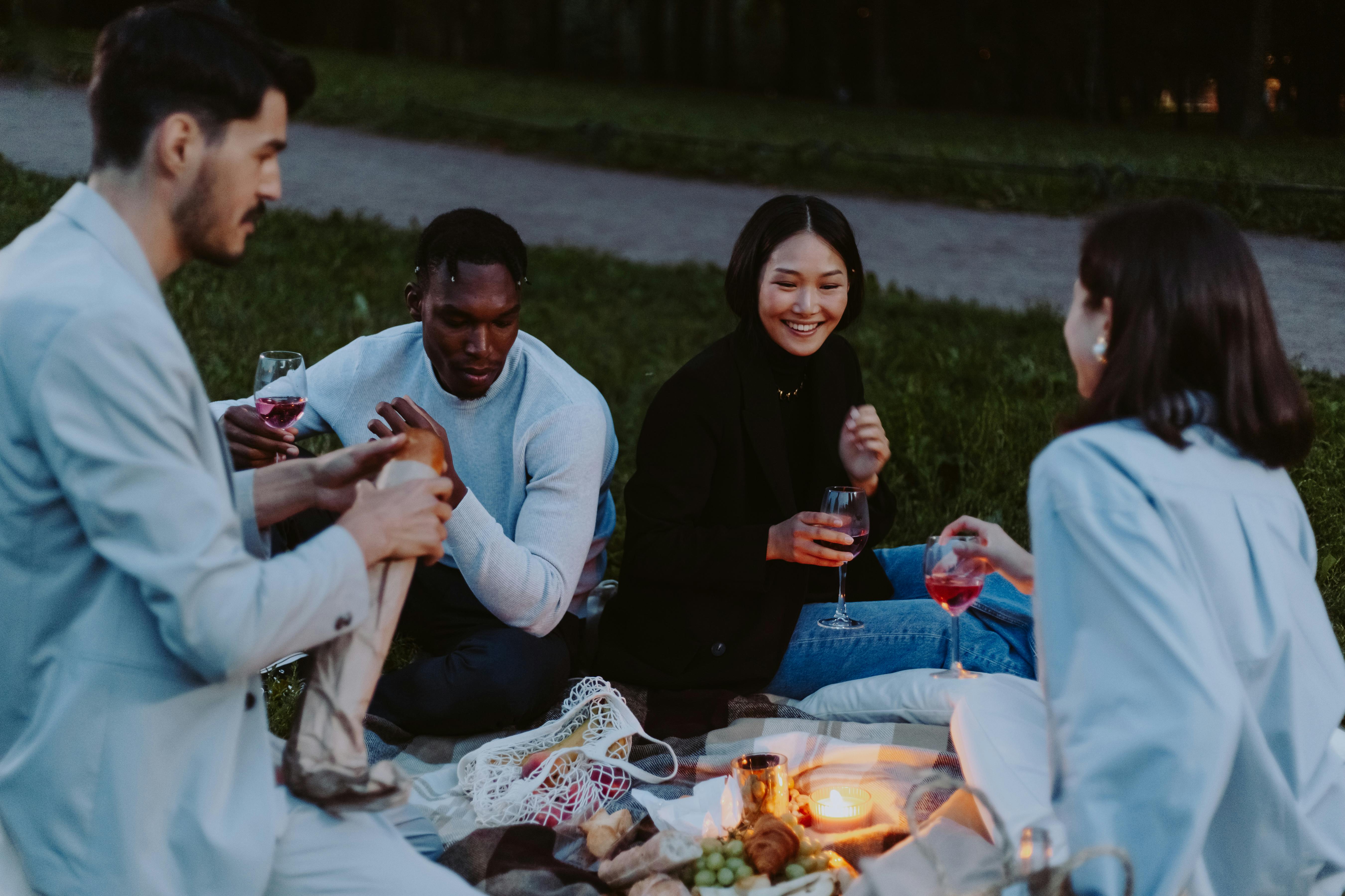 Four people enjoying a picnic outdoors with wine and food.