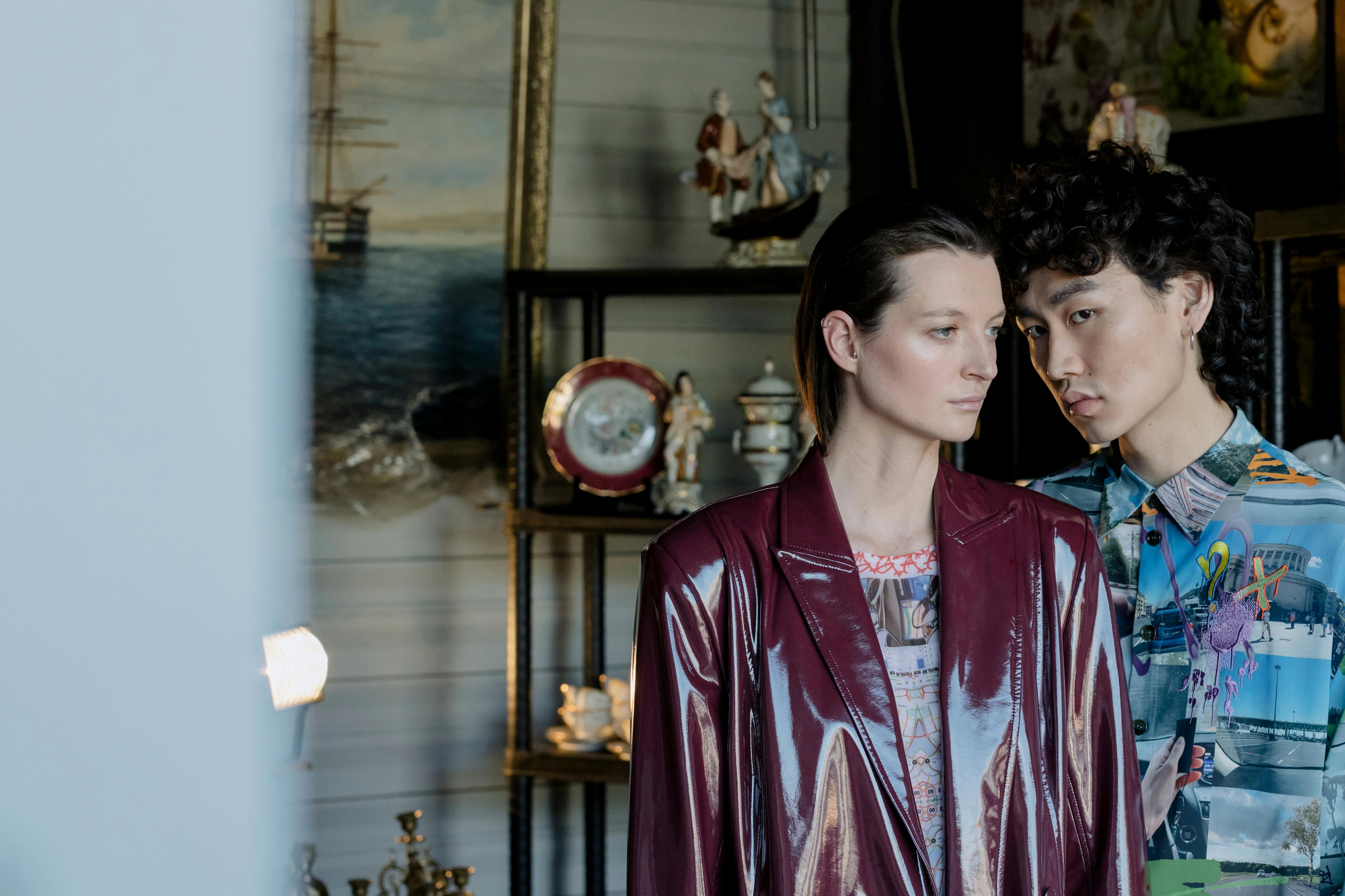 Two people in stylish clothing stand in a room with antiques.