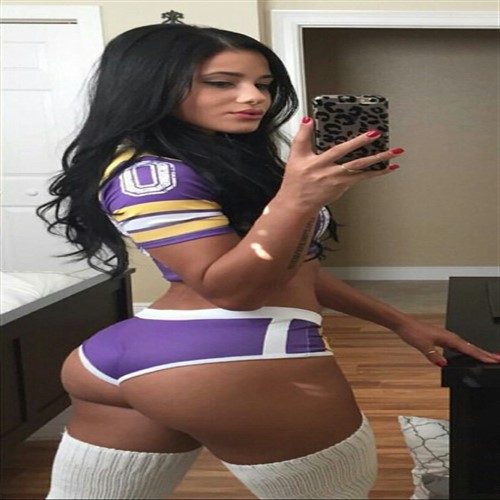 Woman in purple and gold uniform taking a selfie in a bedroom.