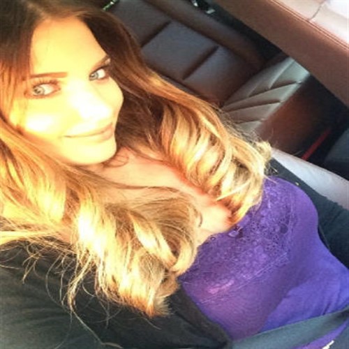 A woman with blonde hair smiles while sitting in a car.