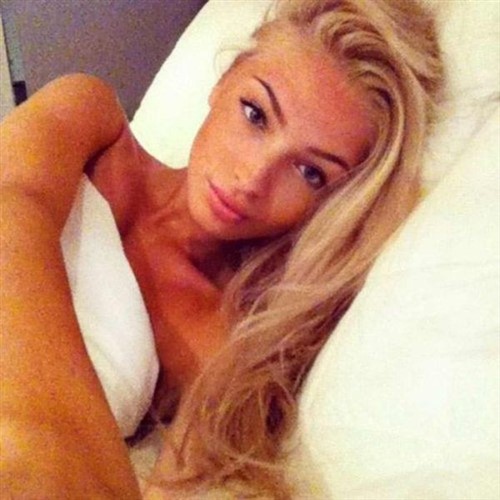 Blonde woman with tan skin lying in bed, looking at the camera.