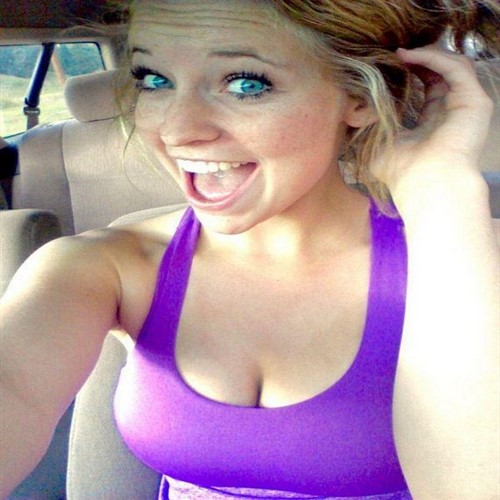 A young woman with bright blue eyes smiles widely in a purple tank top.