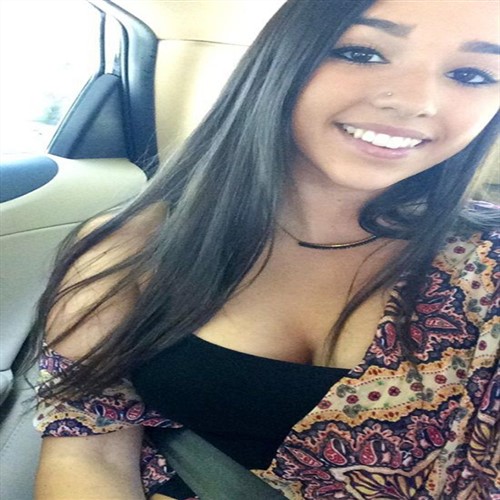 A young cute woman with long dark hair smiles while sitting in a car.