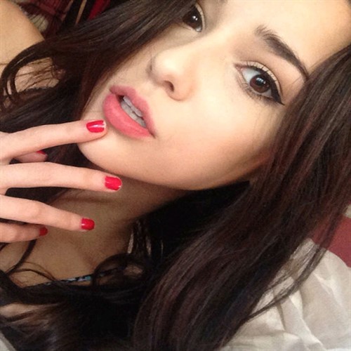 Close-up of a young woman with dark hair, red nails, and pink lipstick.