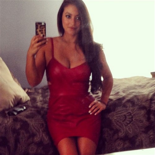 Woman in a red dress takes a selfie in a bedroom.
