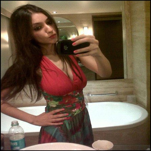 A woman in a red and floral dress takes a selfie in a bathroom.
