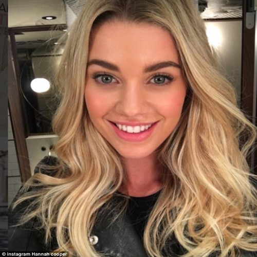Close-up selfie of a smiling blonde woman with blue eyes wearing a black jacket.