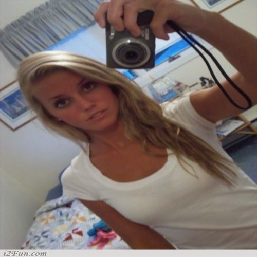A young woman with blonde hair takes a selfie with a digital camera.
